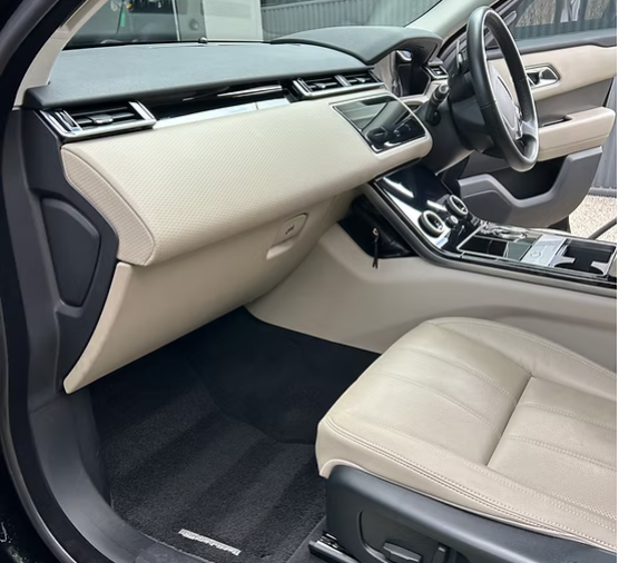 Car interior featuring a beige dashboard, center console, leather seat, and steering wheel.