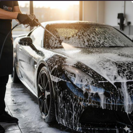 Person washing a black sports car with soap and water in a garage.