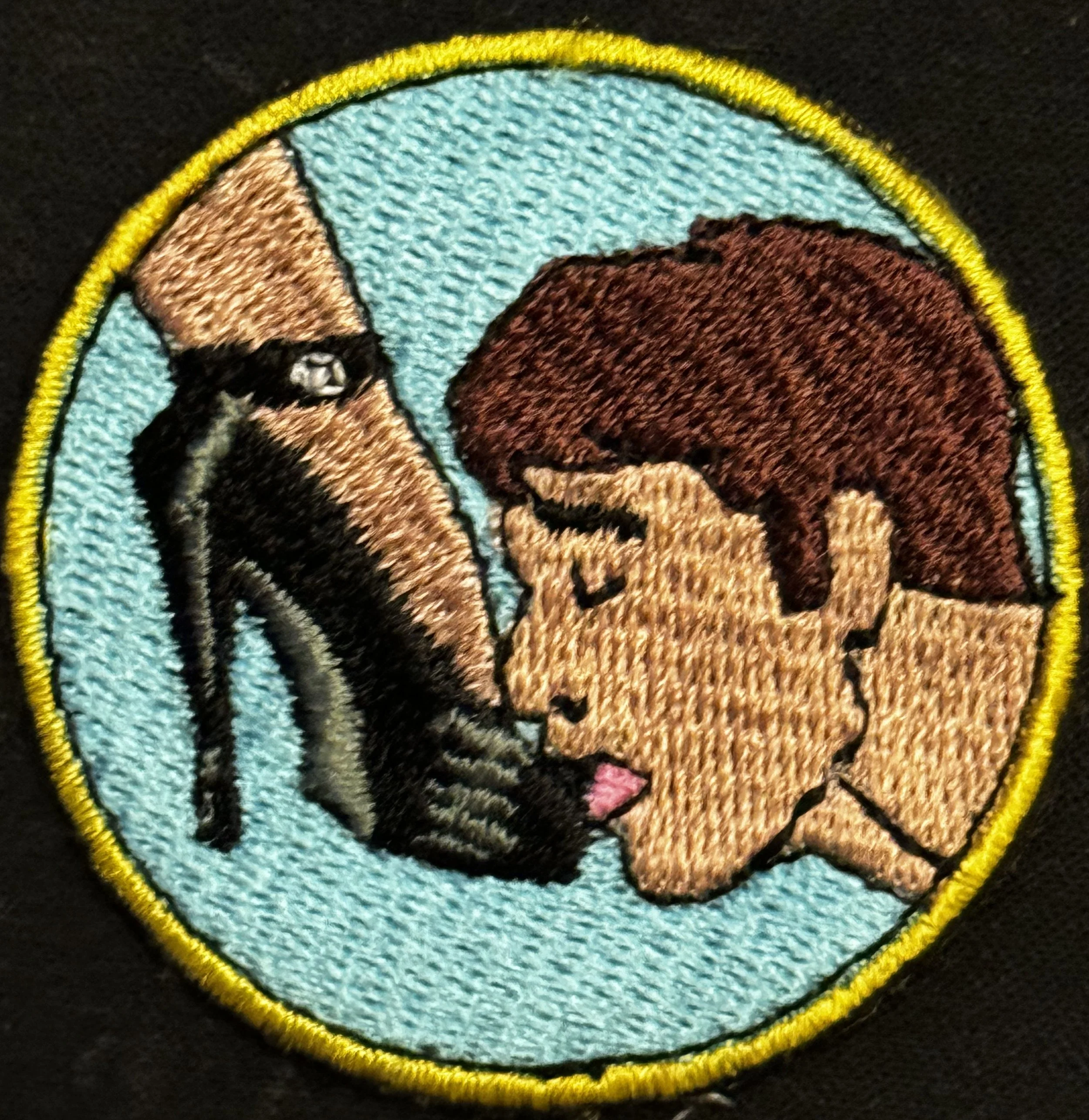 Close-up embroidered patch featuring a wolf's head in profile, set against a circular sky blue background with a yellow border.