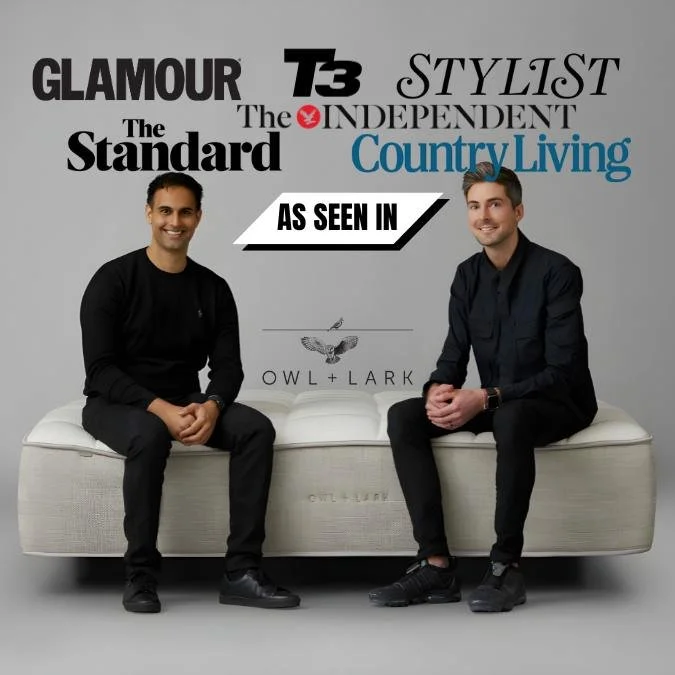 Two men sitting on a mattress with logos of fashion and lifestyle magazines behind them, including Glamour, T3, The Independent, The Standard, and Country Living. The text 'As Seen In' is prominently displayed.