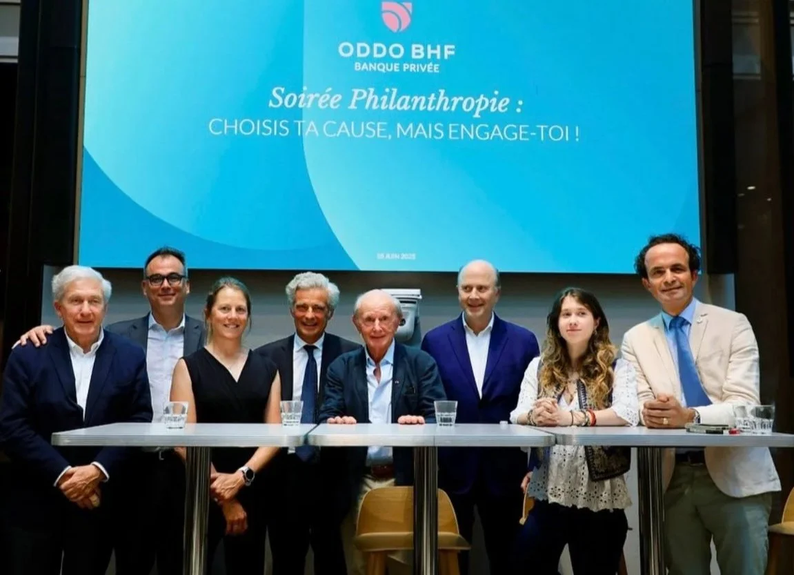 Groupe de huit personnes assises et debout derrière une table, lors d'une soirée philanthropique organisée par ODDO BHF, avec un grand écran derrière affichant le logo de la banque et le texte en français.