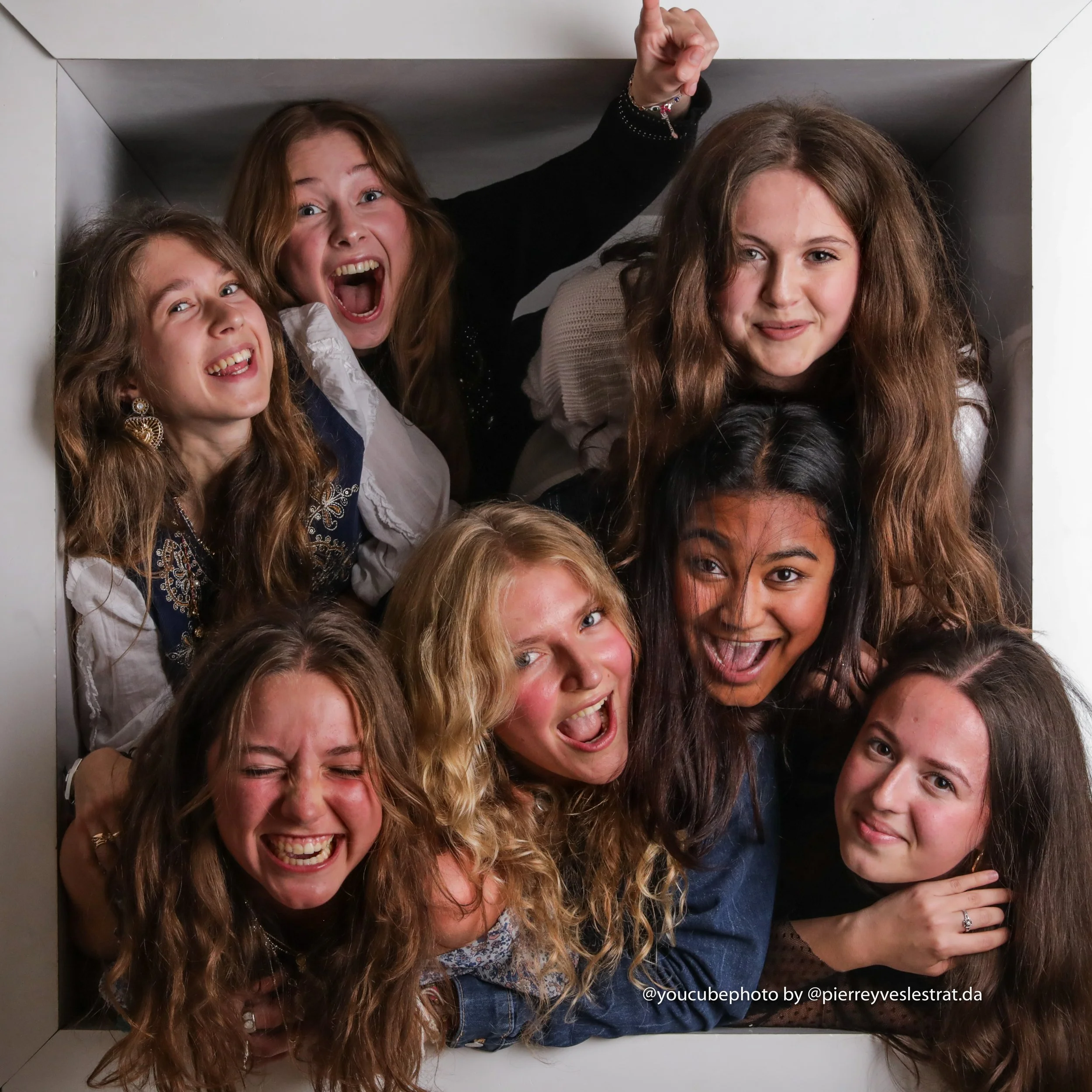 Groupe de jeunes femmes souriantes et amusantes posant dans une cabine d'essayage ou un espace confiné, s'amusant et montrant de diverses expressions joyeuses.