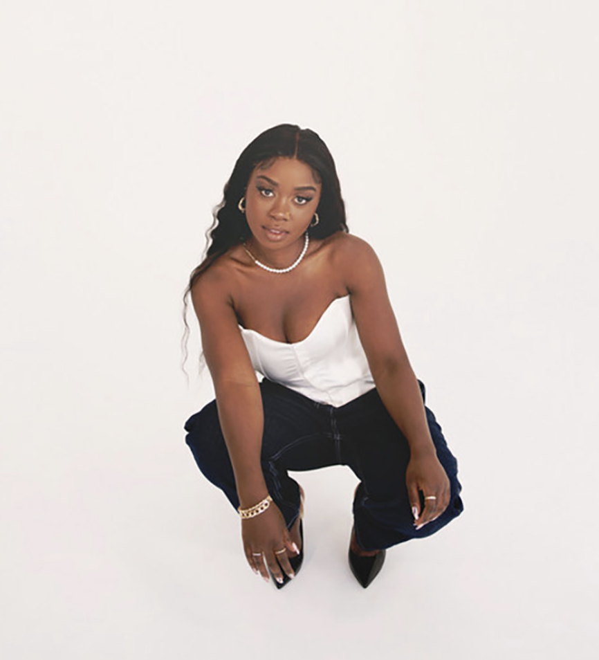 Jeune femme en pose de mode, portant un haut blanc, des pantalons noirs et des accessoires, contre un fond blanc.