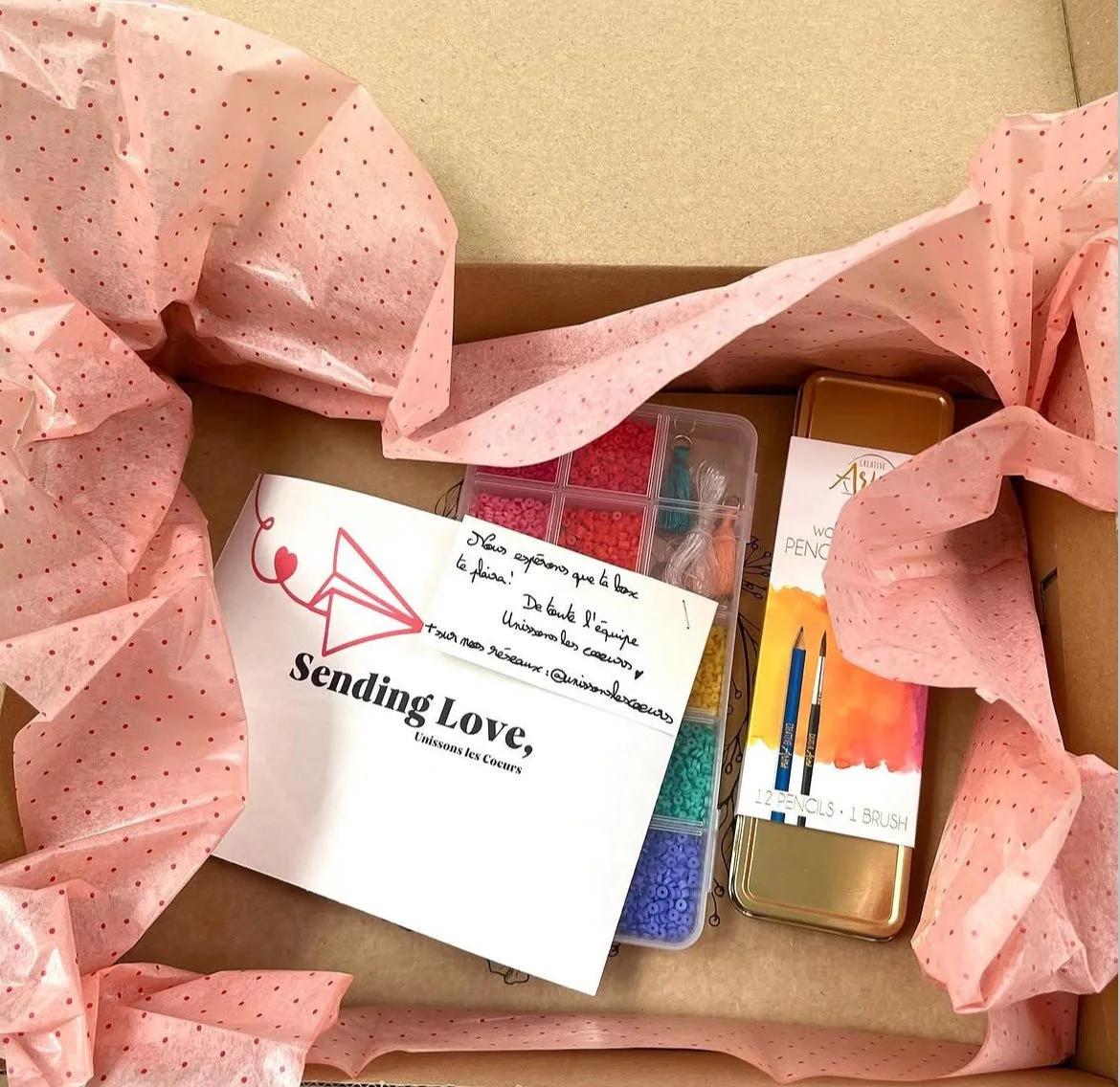 Kit de couture dans une boîte en carton, comprenant des fils, des aiguilles, des crayons et une note manuscrite.
