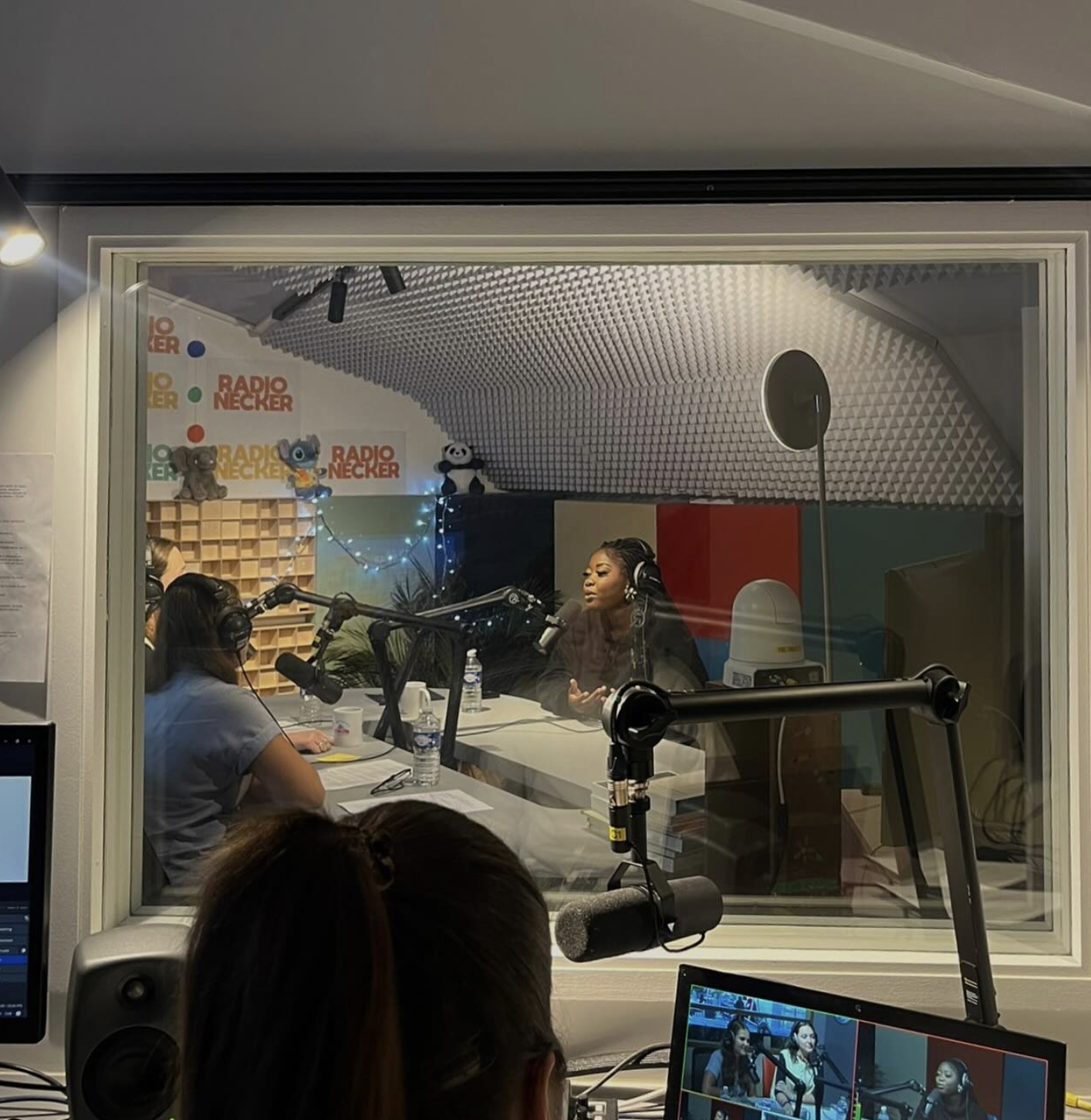 Une salle d'enregistrement radio avec plusieurs personnes, des microphones, un décor avec des peluches et des panneaux Radio Necker.