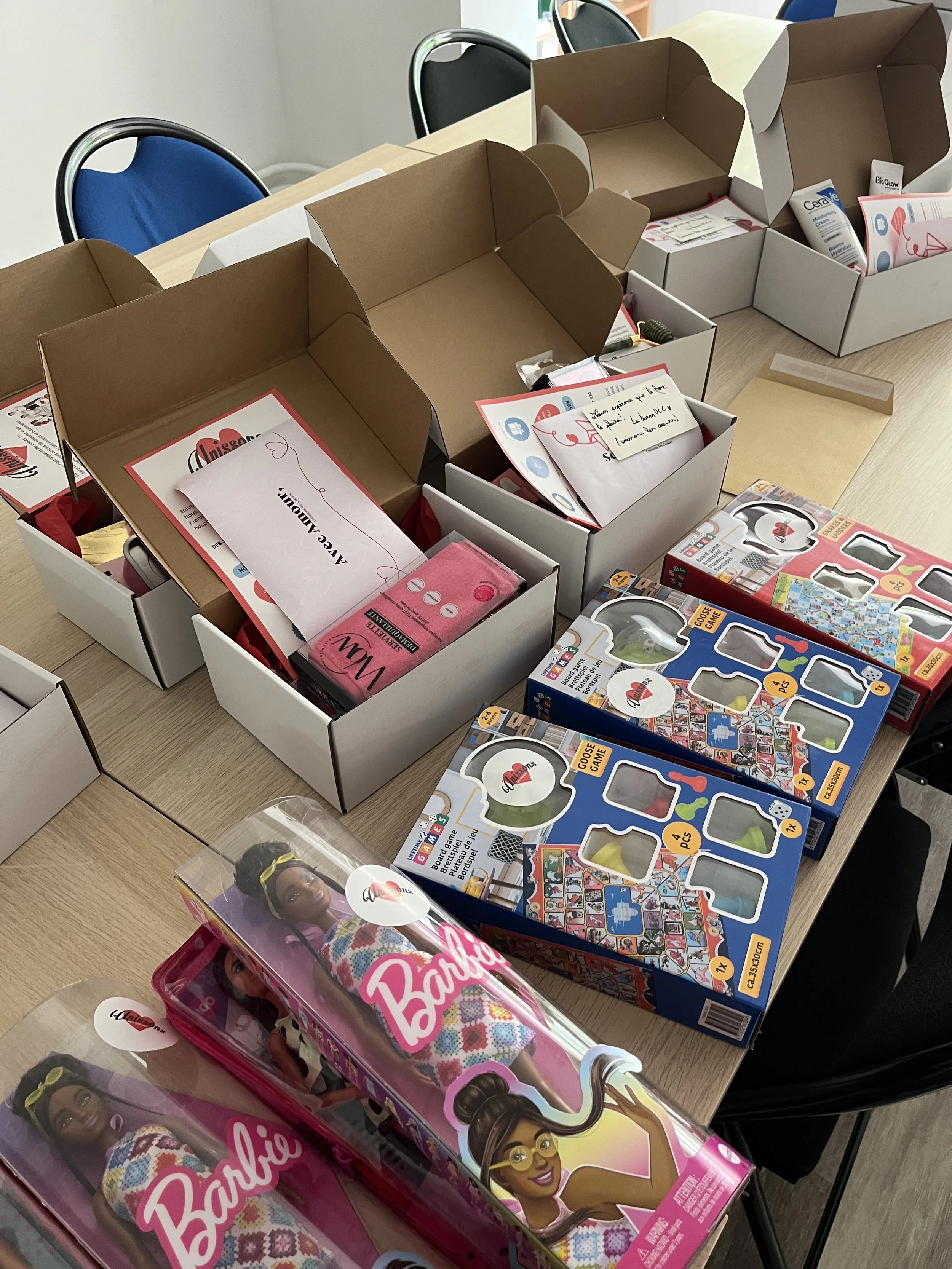Une table avec plusieurs boîtes contenant des jouets et des accessoires, notamment des poupées Barbie, jouets de société et autres articles de jeu.