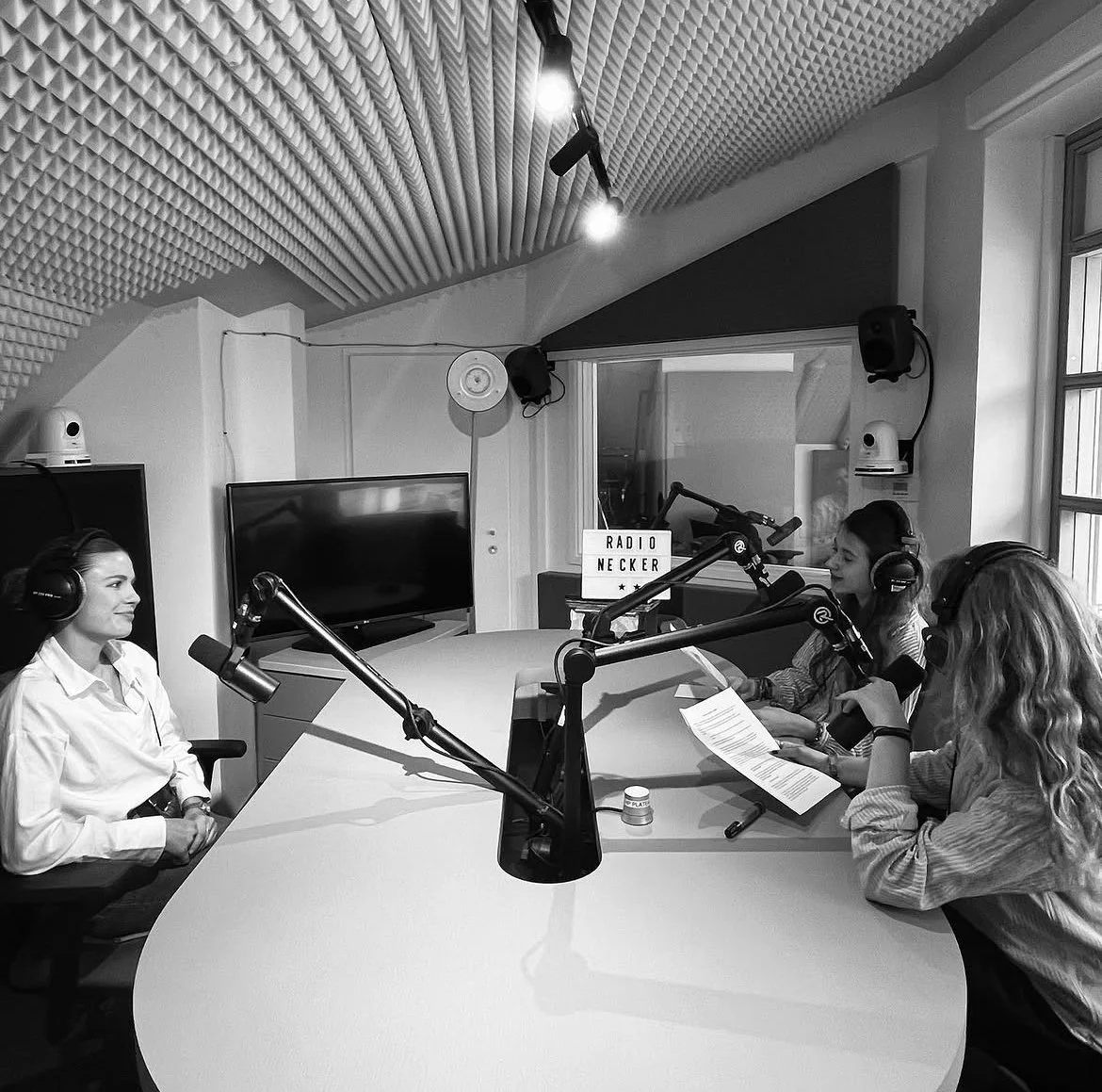 Trois femmes dans un studio d'enregistrement radio, assises autour d'une table ronde avec des microphones et des écouteurs.