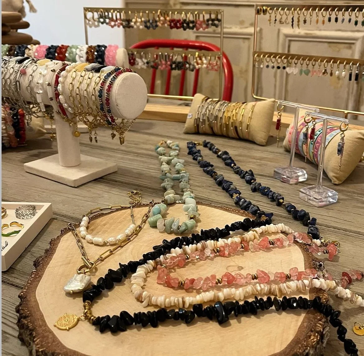 Collection de bijoux en perles et en or, comprenant des colliers, bracelets et boucles d'oreilles, exposés sur un meuble en bois avec des miroirs et coussins