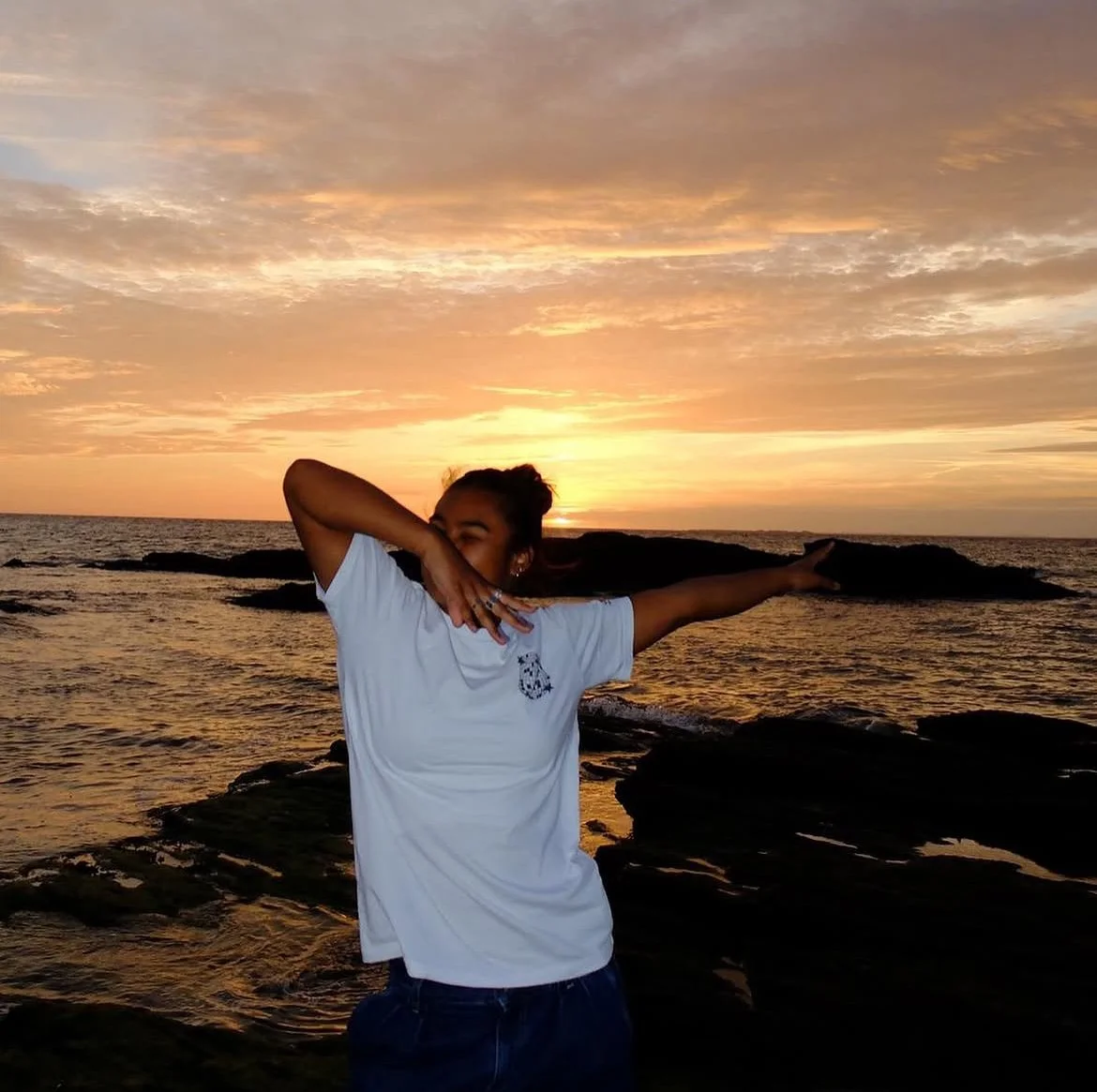 Une femme debout sur la plage lors d'un coucher de soleil, faisant une pose artistique avec la mer en arrière-plan.