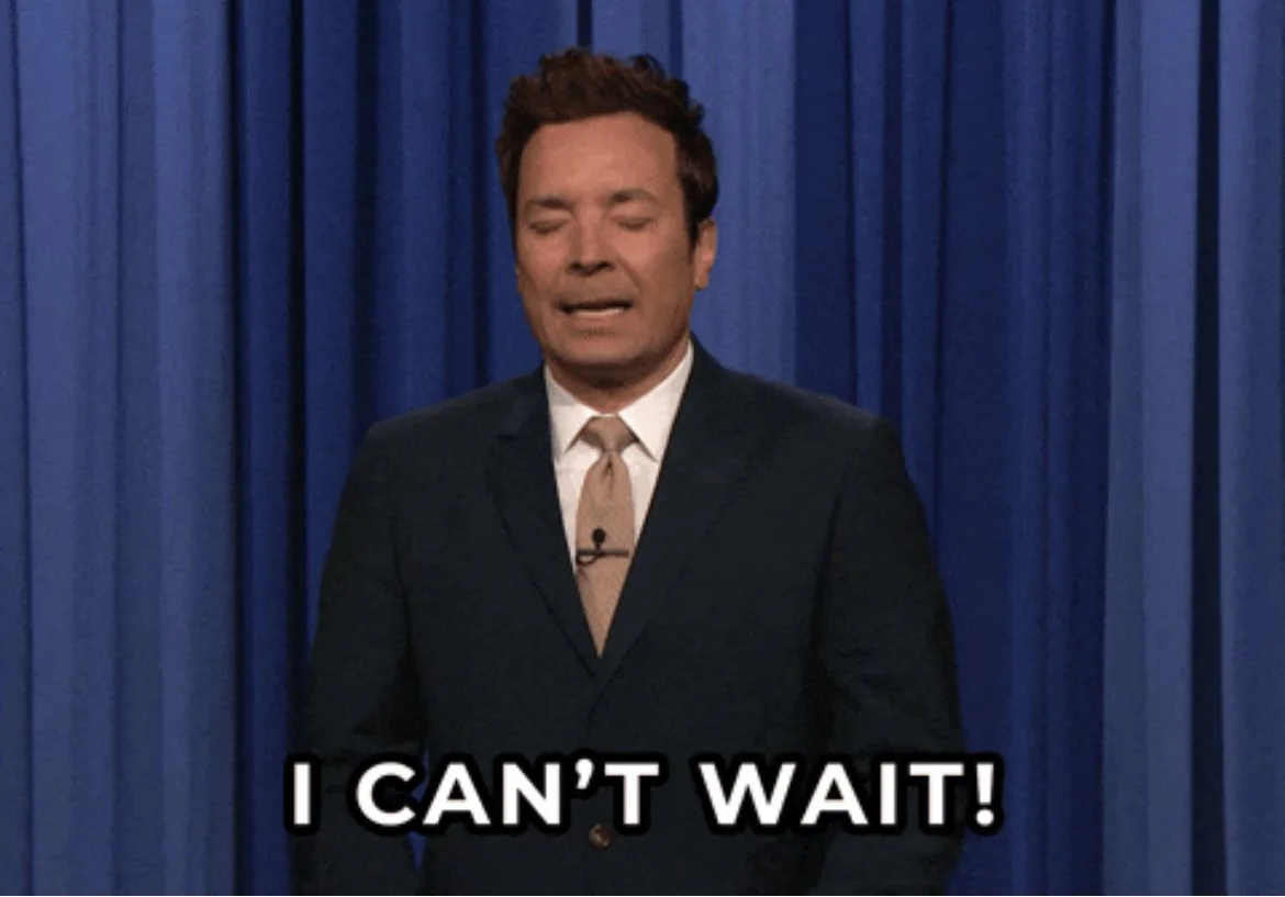 Un homme en costume noir avec une cravate beige, avec les yeux fermés, exprimant une impatience ou une excitation, devant un rideau bleu. Texte en dessous : "I CAN'T WAIT!".