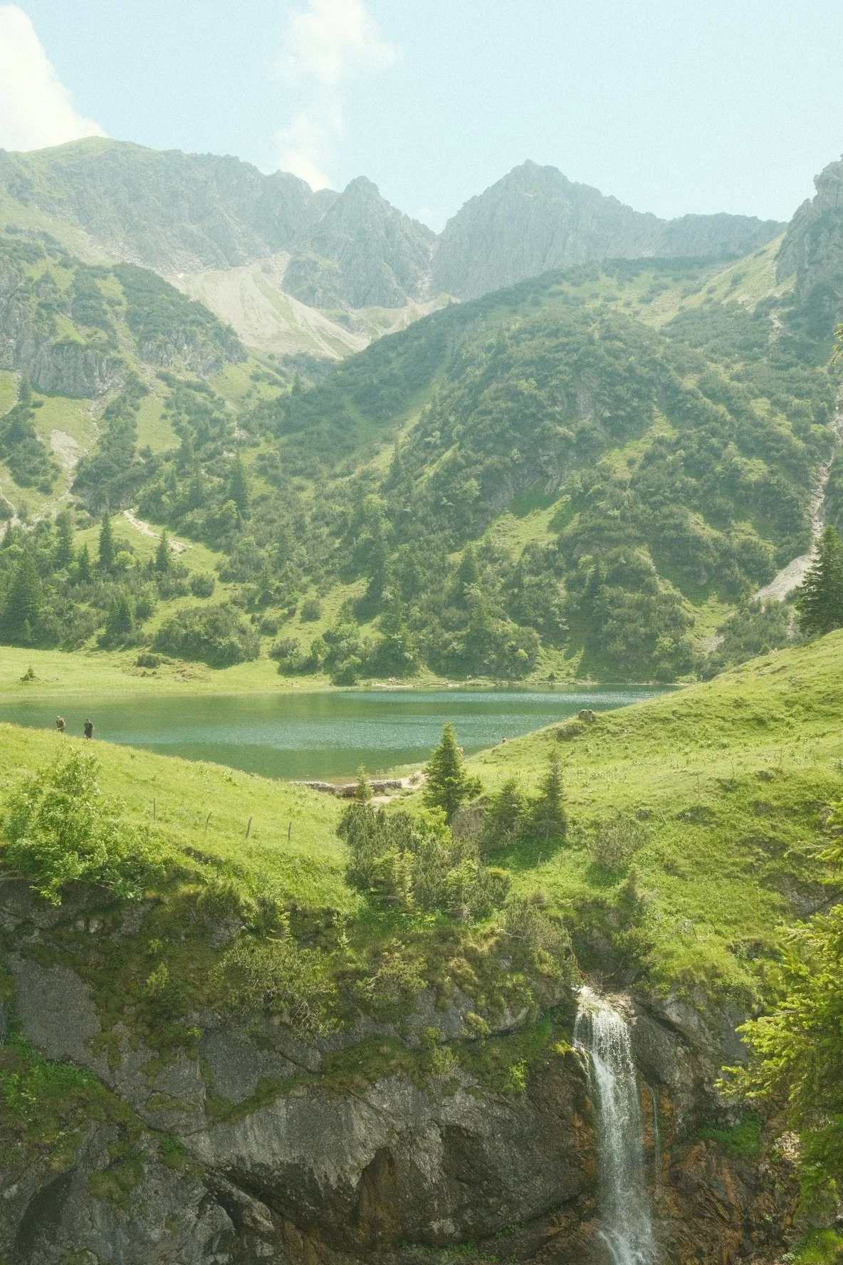 A mountain landscape with green hills, a lake, and a waterfall in a lush valley.