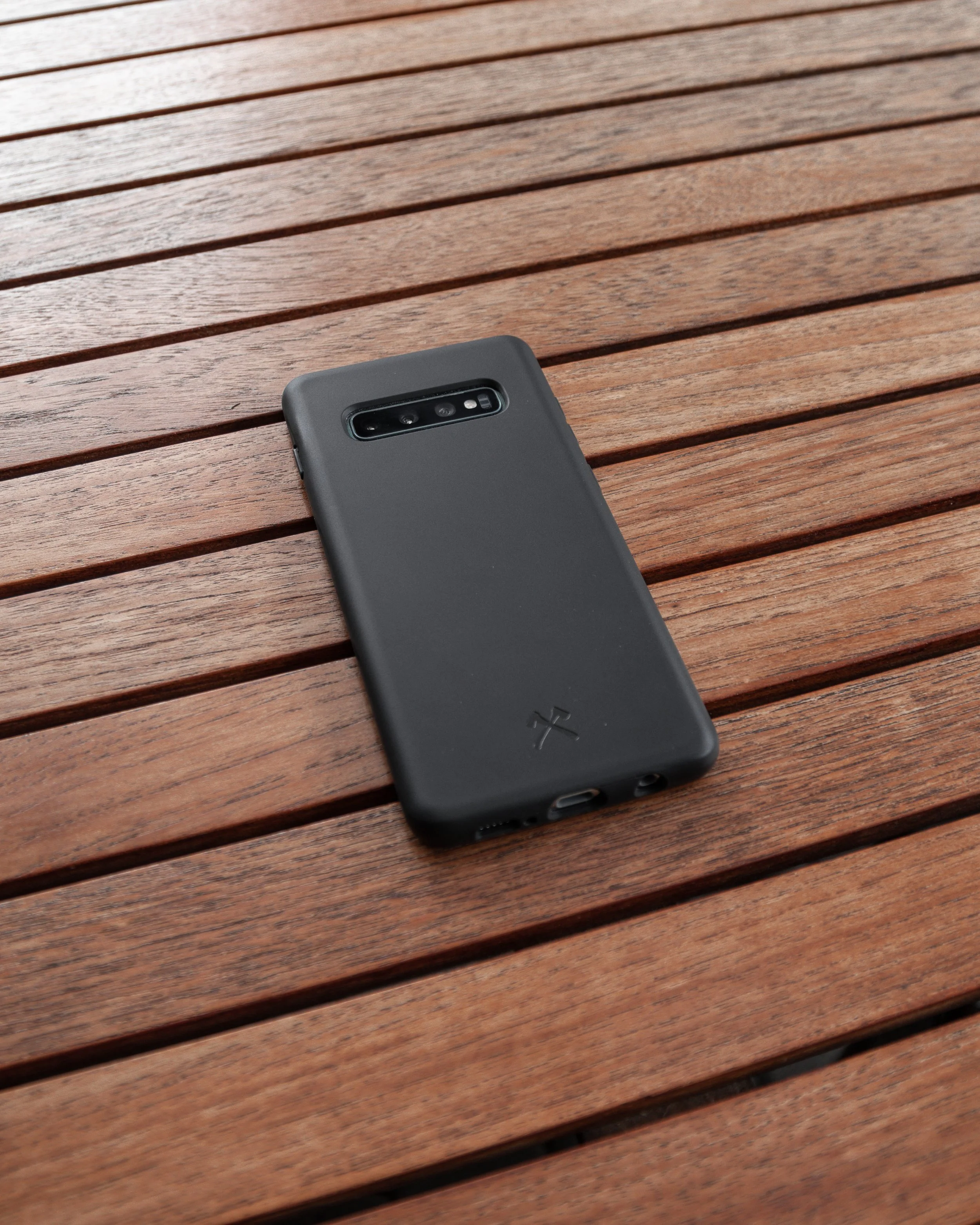 Black smartphone with triple camera setup placed on wooden slatted surface.
