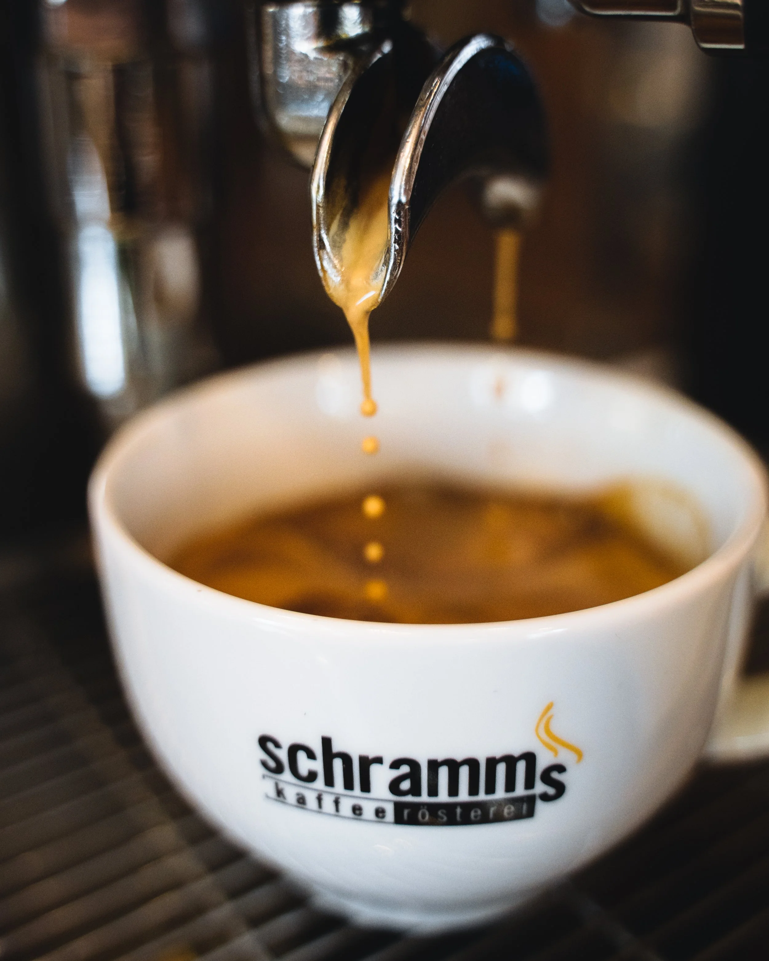 Close-up of coffee being poured from a coffee maker into a mug with the logo 'Schramms Kaffee-Försterei' on it.