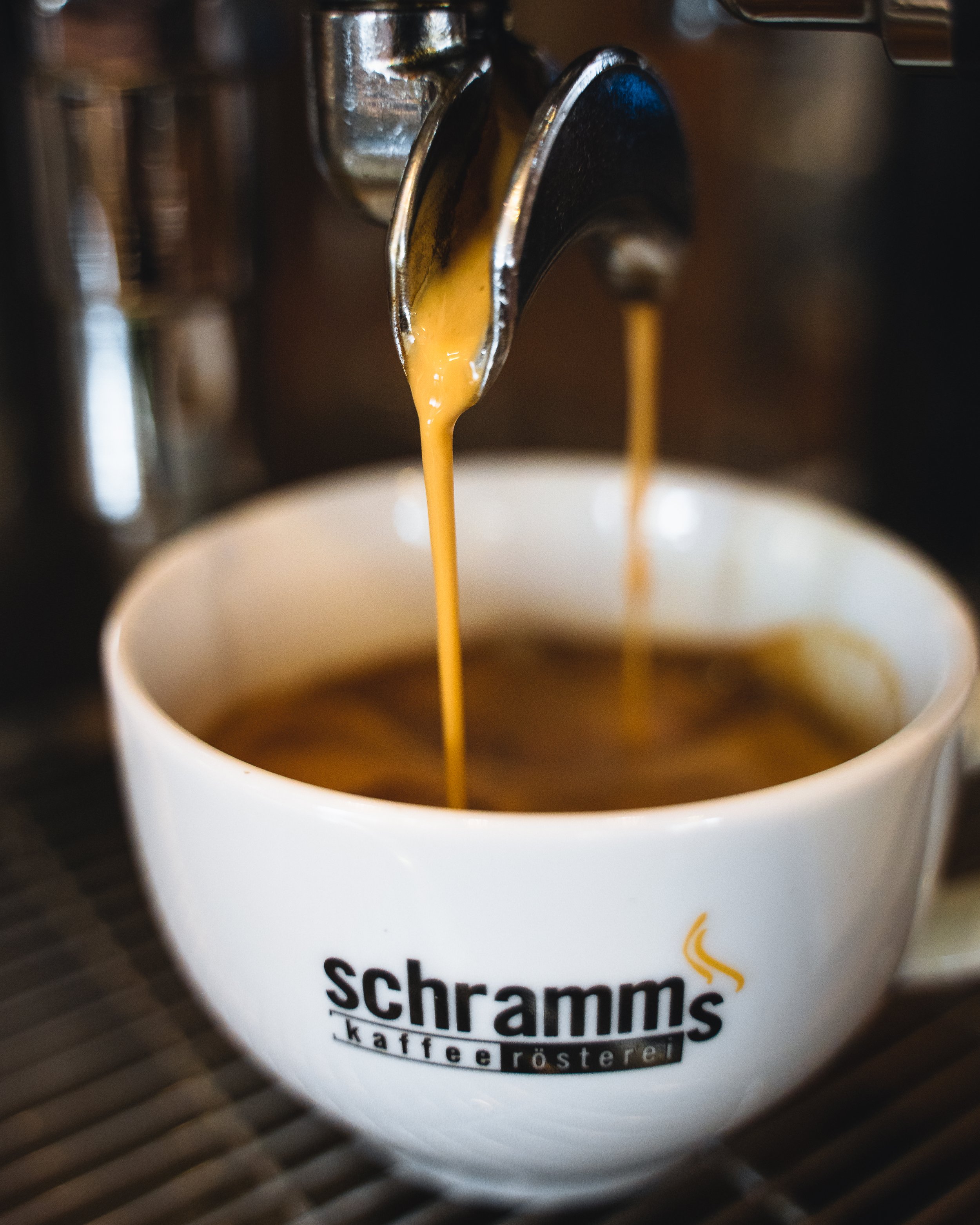 Close-up of a coffee machine pouring espresso into a white cup with part of a logo visible on the cup.