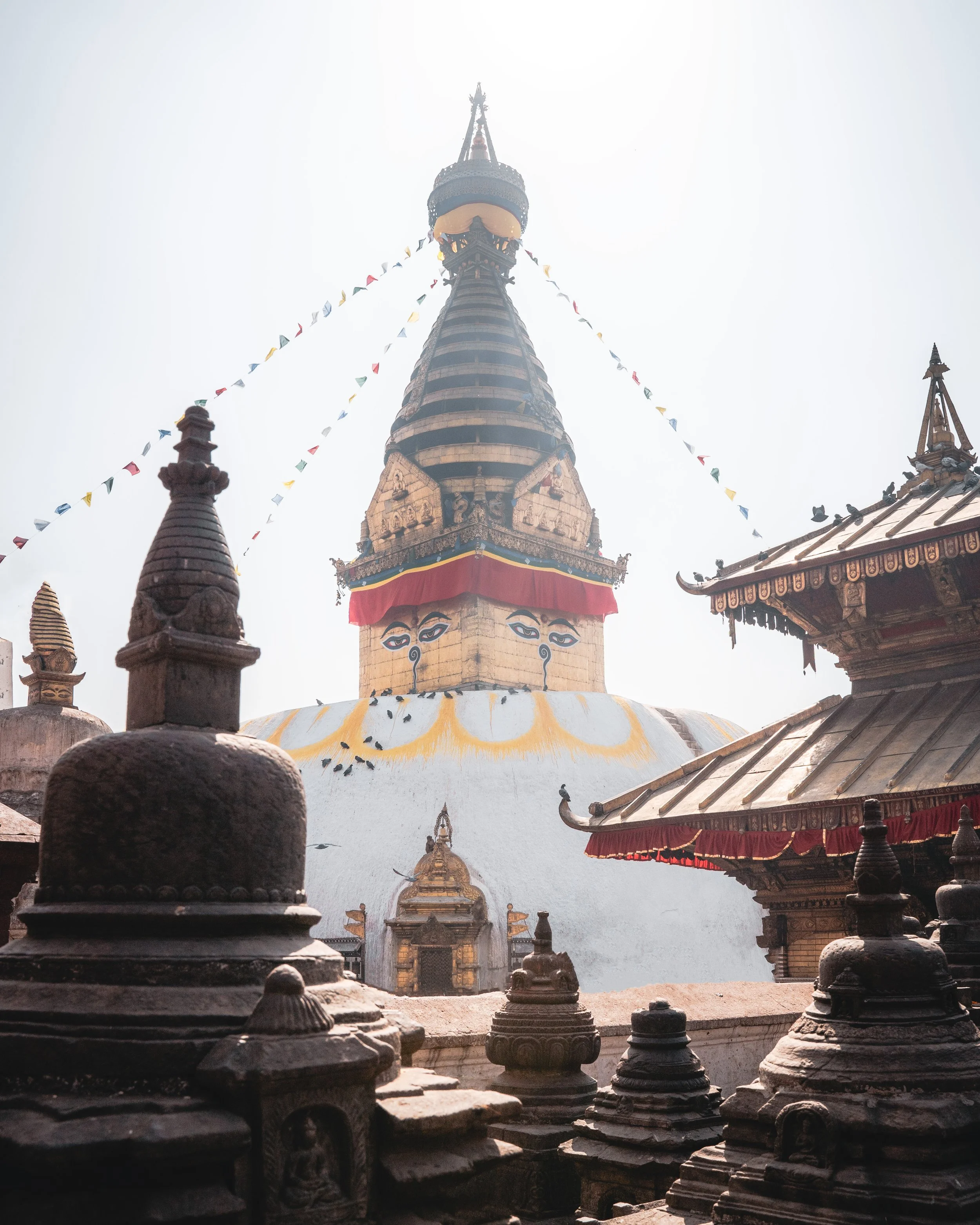 View of a Buddhist stupa with a golden spire, surrounded by smaller shrines and structures, under a bright sky.