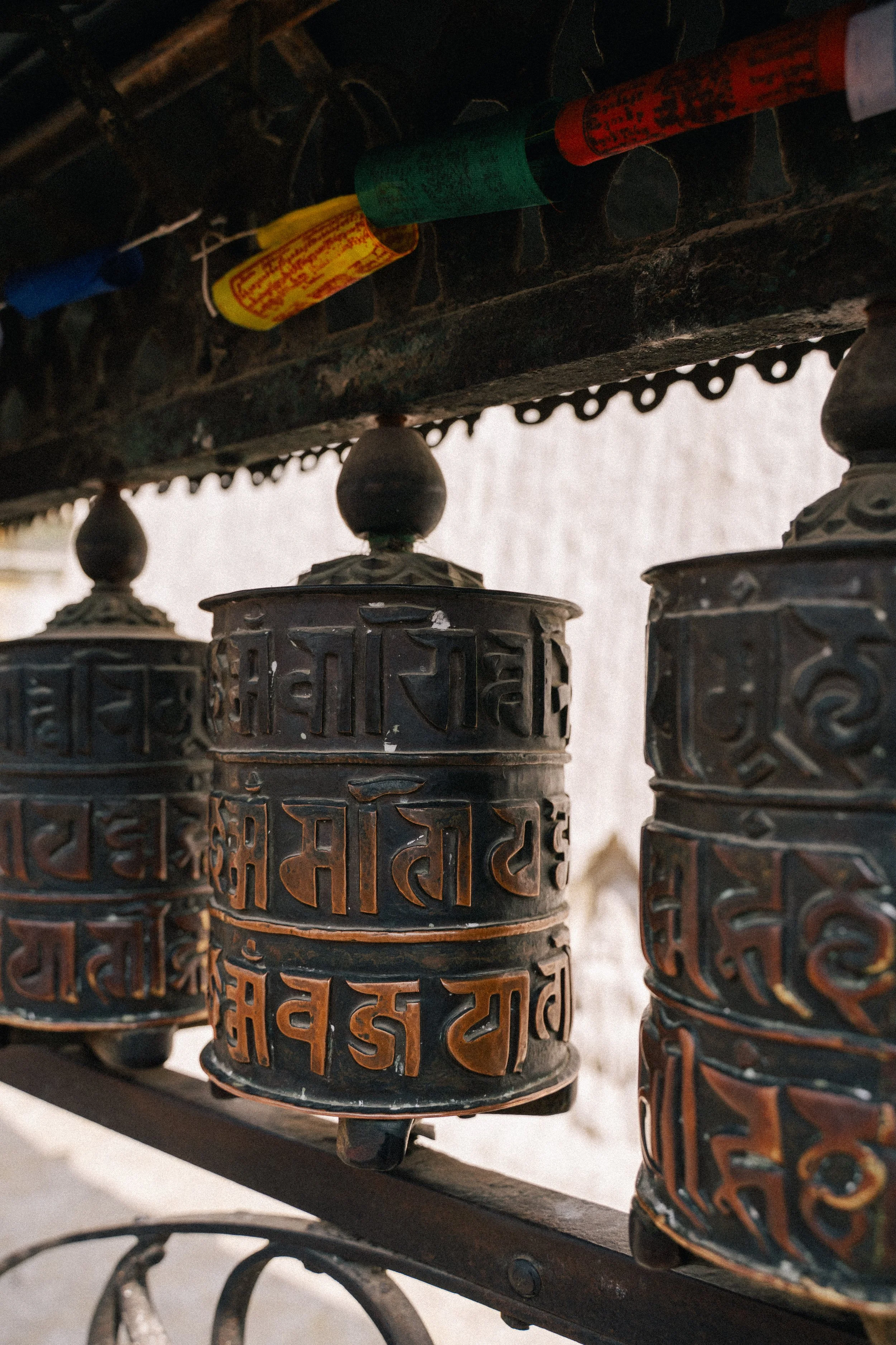 Close-up of metal prayer wheels with intricate carvings and inscriptions in a Buddhist temple, mounted on a horizontal rod.