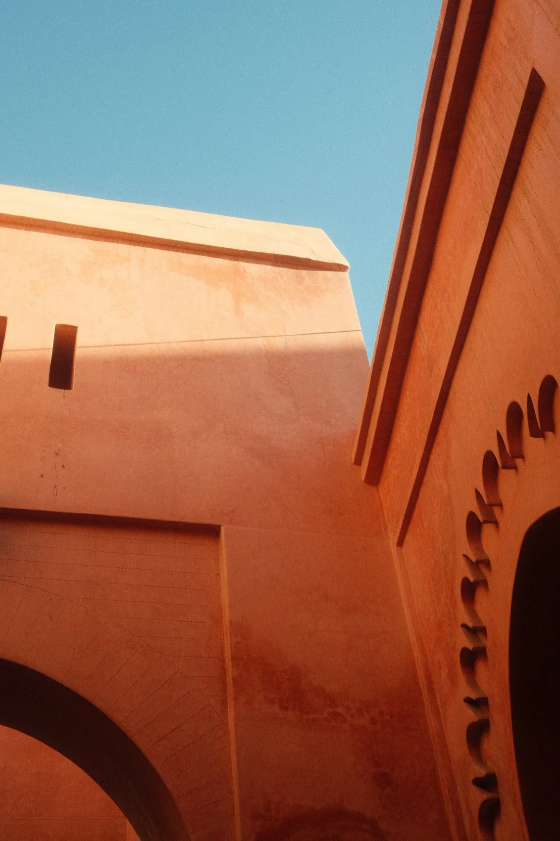 Looking up at a building with a blue sky background. The building has beige and orange-colored walls with architectural details and cutouts.