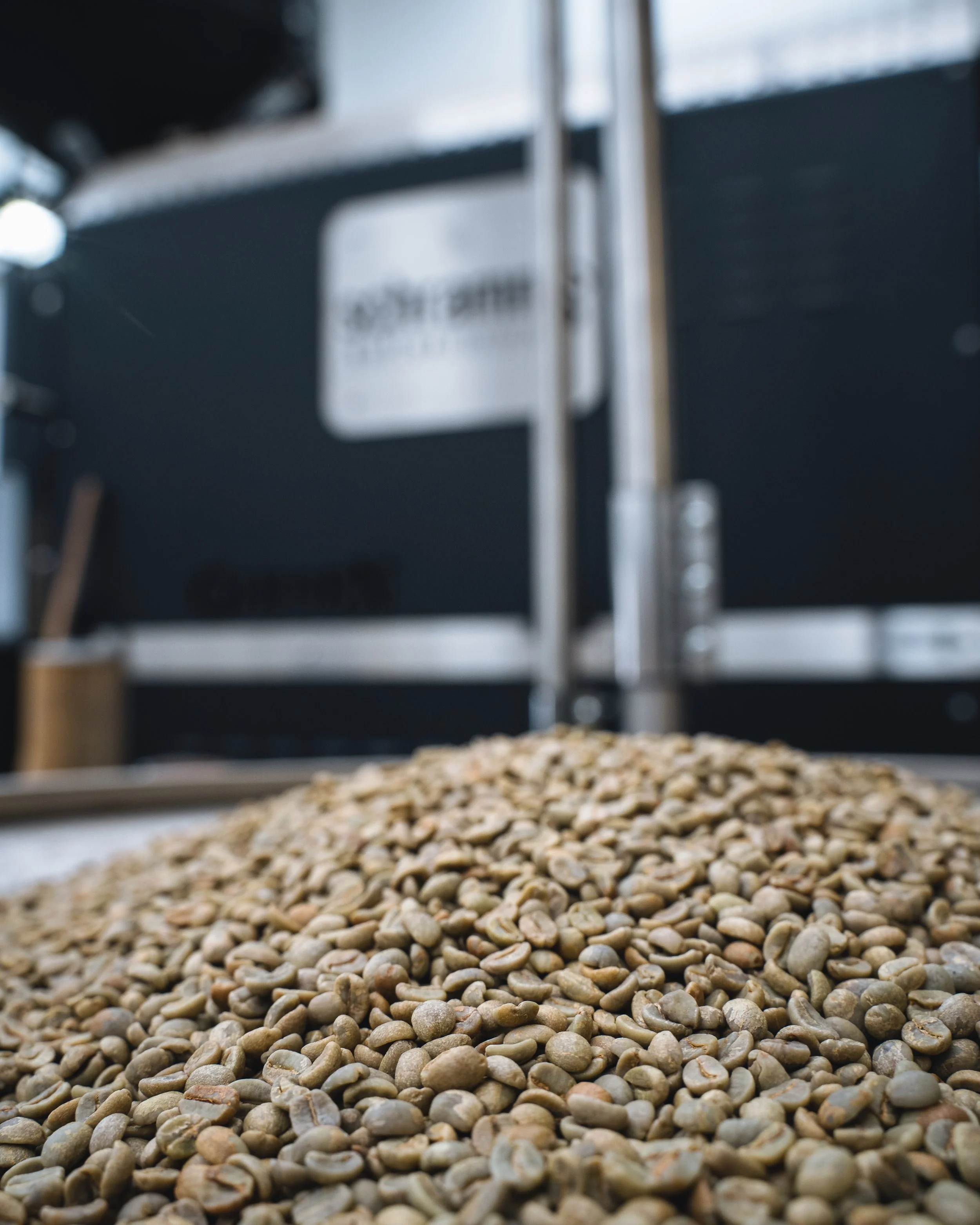 Close-up view of a pile of green coffee beans on a tray with a blurred background.