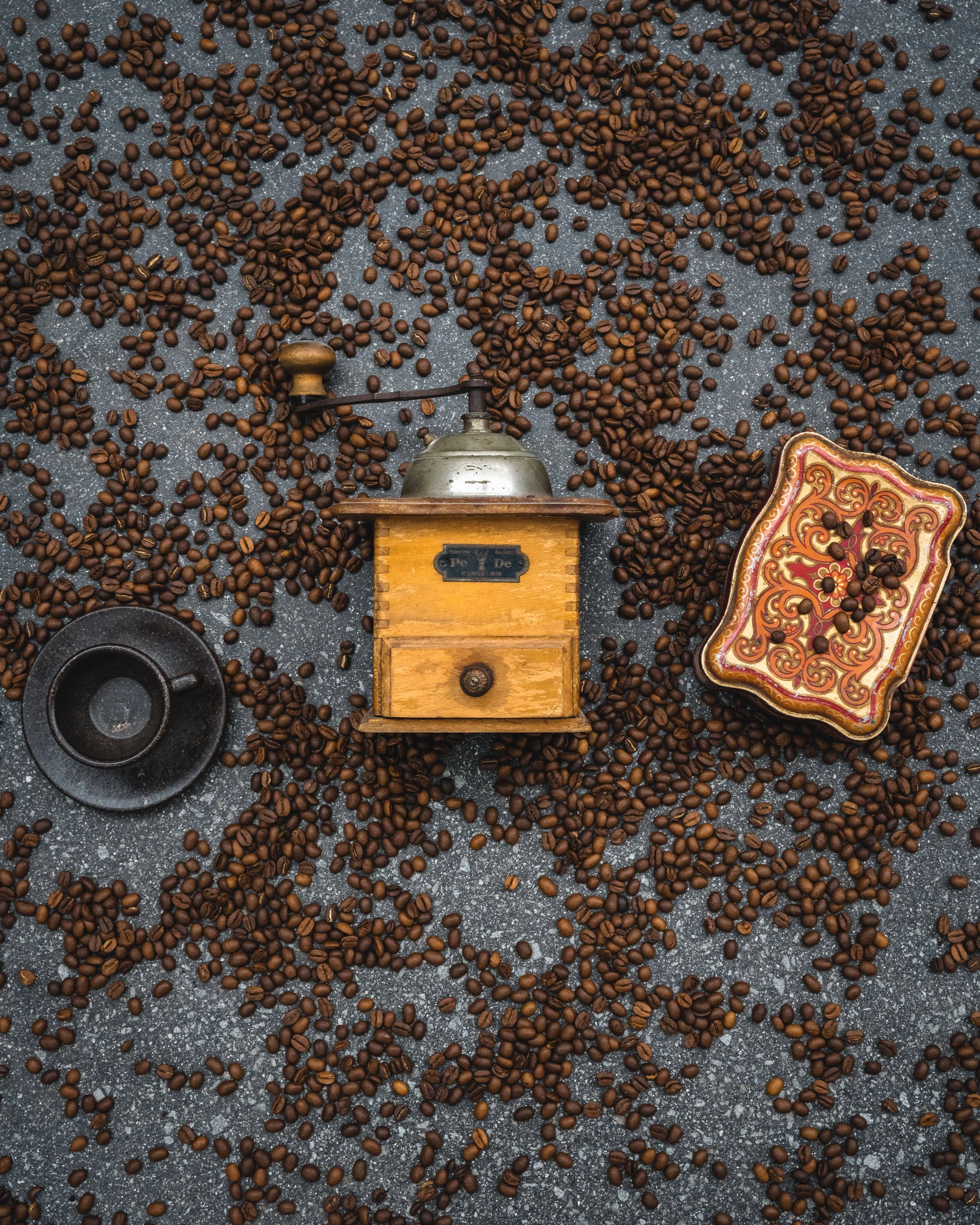 Coffee beans scattered on a flat surface with a vintage coffee grinder and a decorative box nearby.