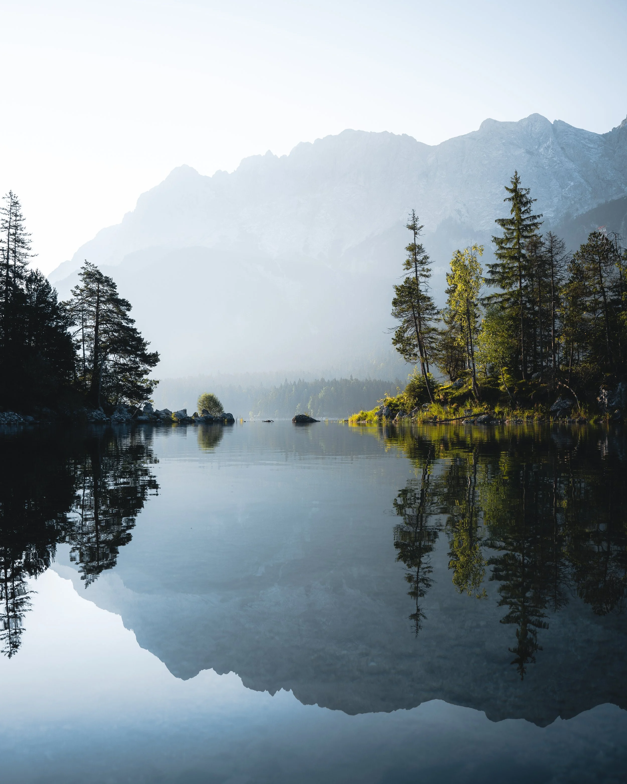Mountain landscape with evergreen trees near a calm lake reflecting the mountains and trees.