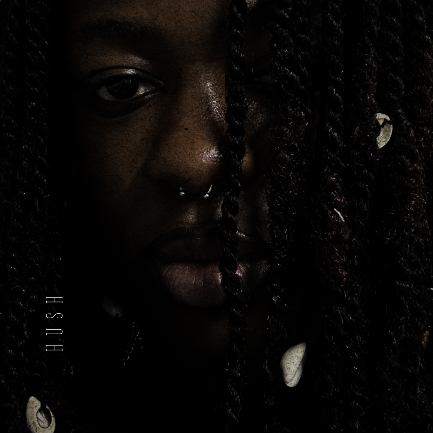 Close-up portrait of a woman with dark skin and curly hair, with one eye visible, a septum ring, and shells in her hair and necklace.
