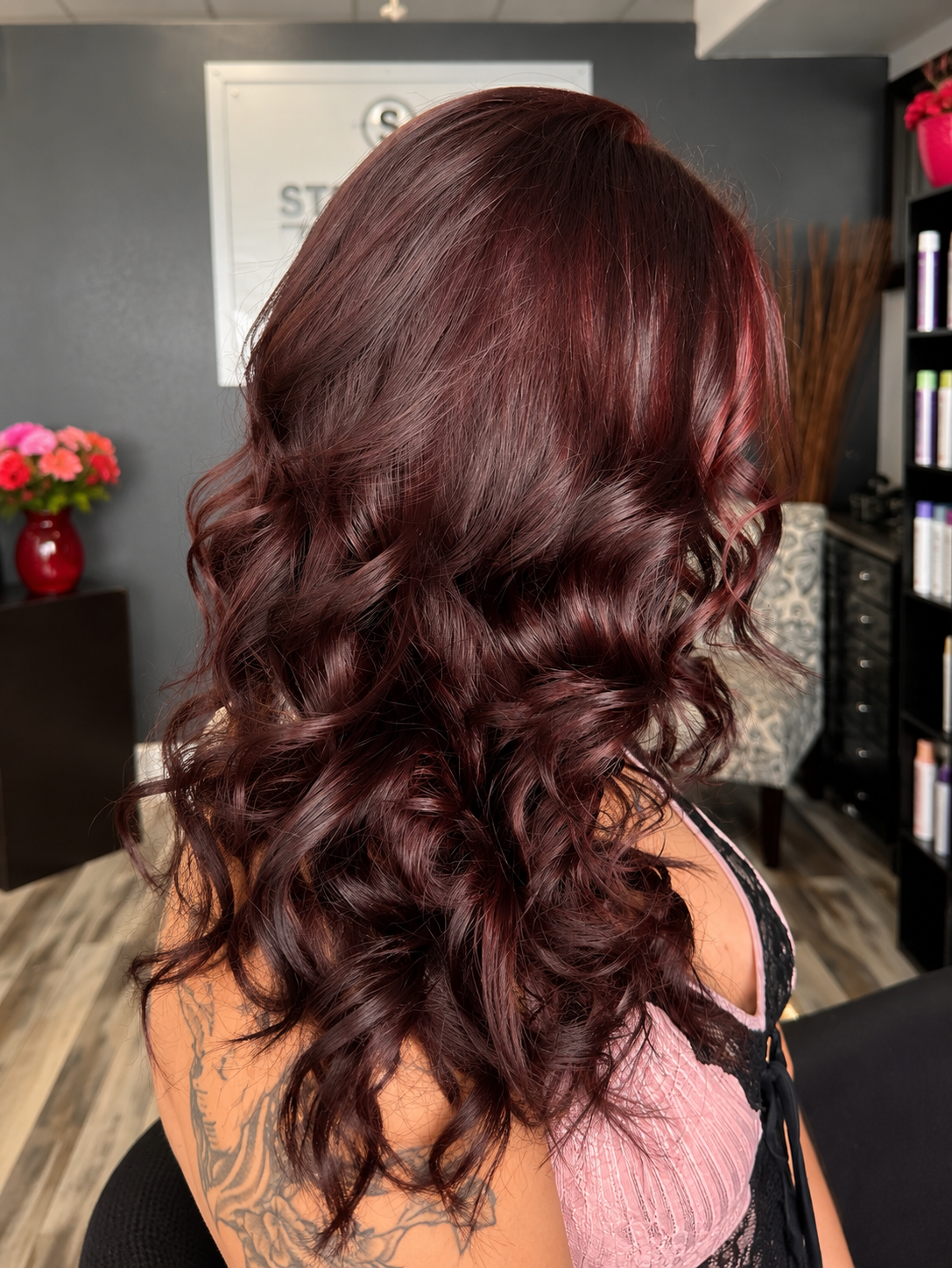 Side view of a woman with long, burgundy, curly hair in a salon setting.