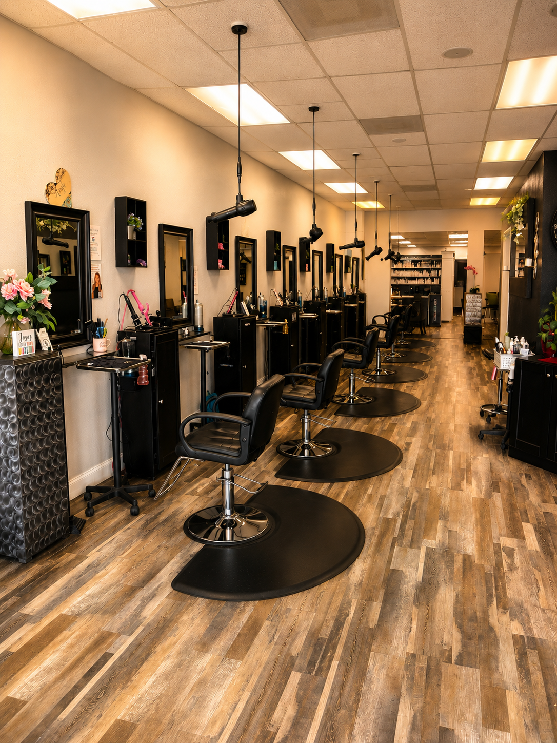 Interior of a hair salon with multiple styling stations, black swivel chairs, mirrors, and hairdressing tools. Wooden flooring and drop ceiling lights are visible.
