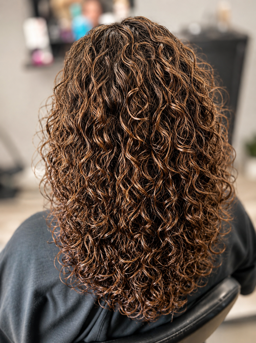 Back of a person with brown, curly, wet hair in a salon setting.