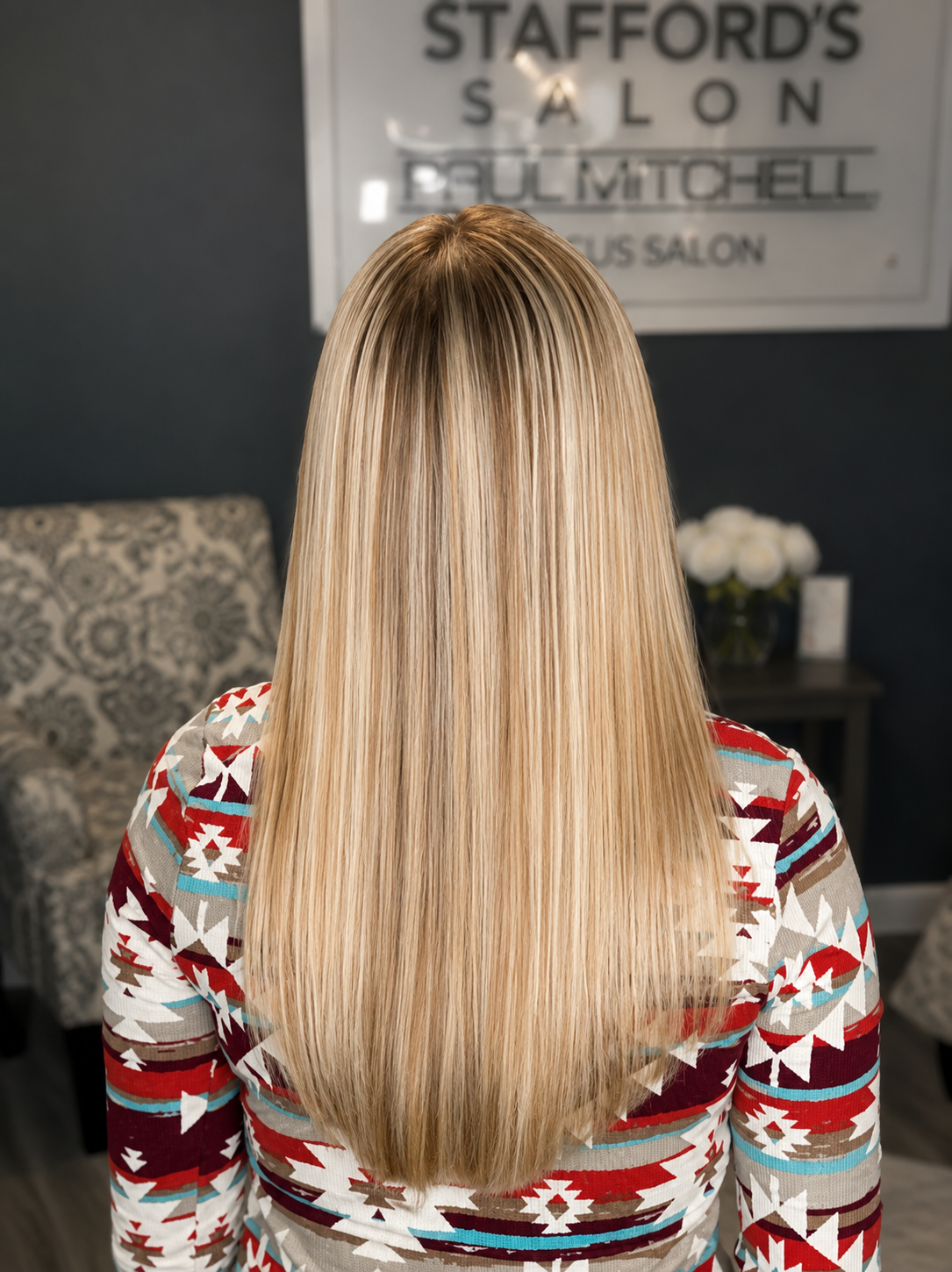 Back view of a woman with long, straight blonde hair at a salon, with a sign in the background reading 'Stafford's Salon'.