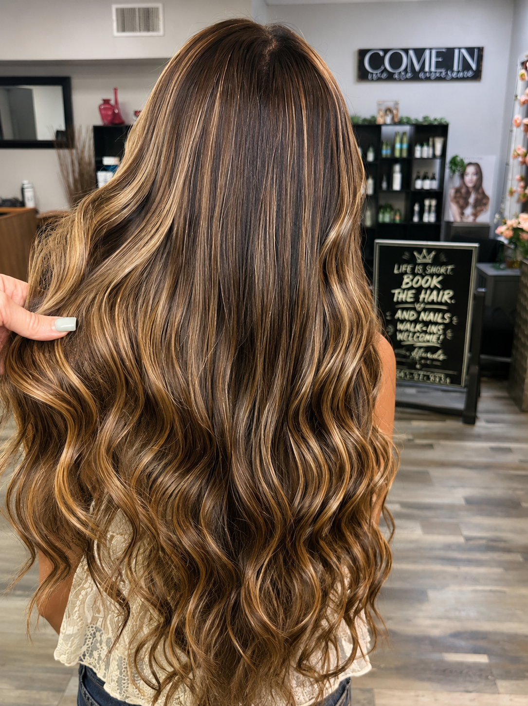 Rear view of a woman with long, wavy, brown hair with blonde highlights in a salon.