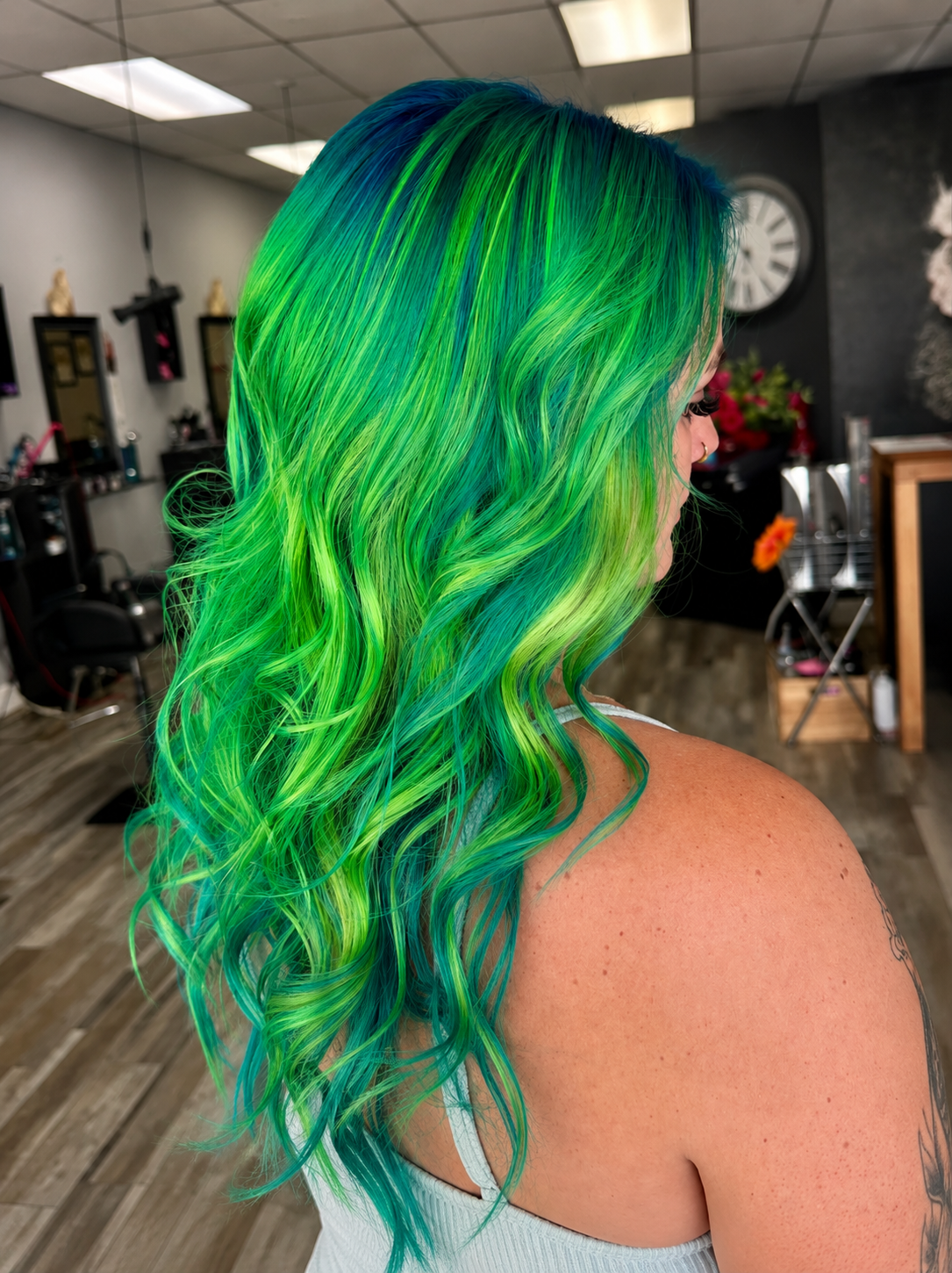 Woman with vibrant green and blue curly hair in a salon setting.