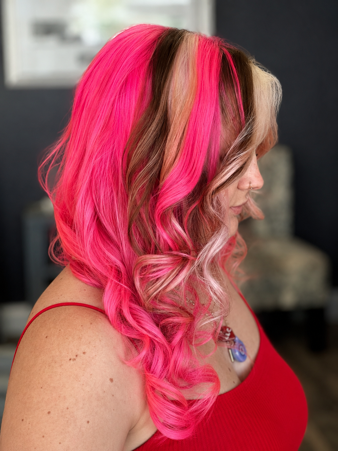 A woman with long, wavy hair dyed in vibrant shades of pink and blonde, wearing a red tank top.