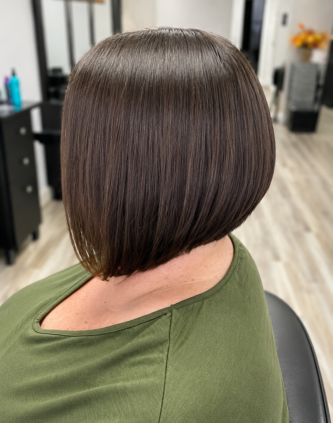 A woman with a freshly styled, sleek, dark brown bob haircut sitting in a salon chair.