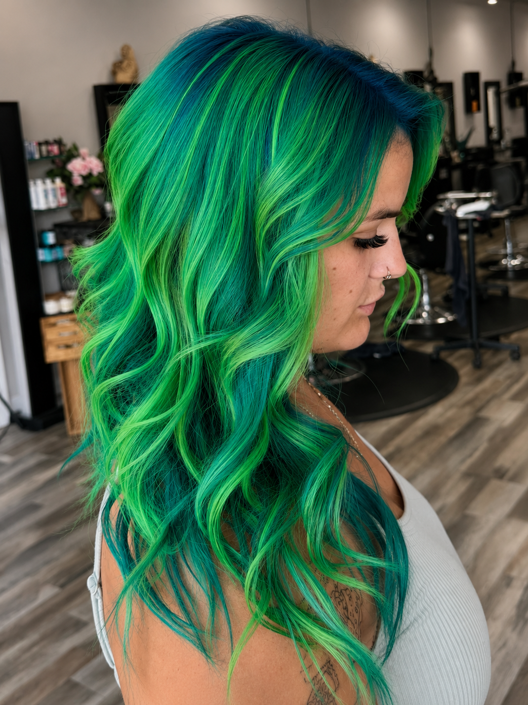 A woman with vibrant green and blue wavy hair in a salon setting.