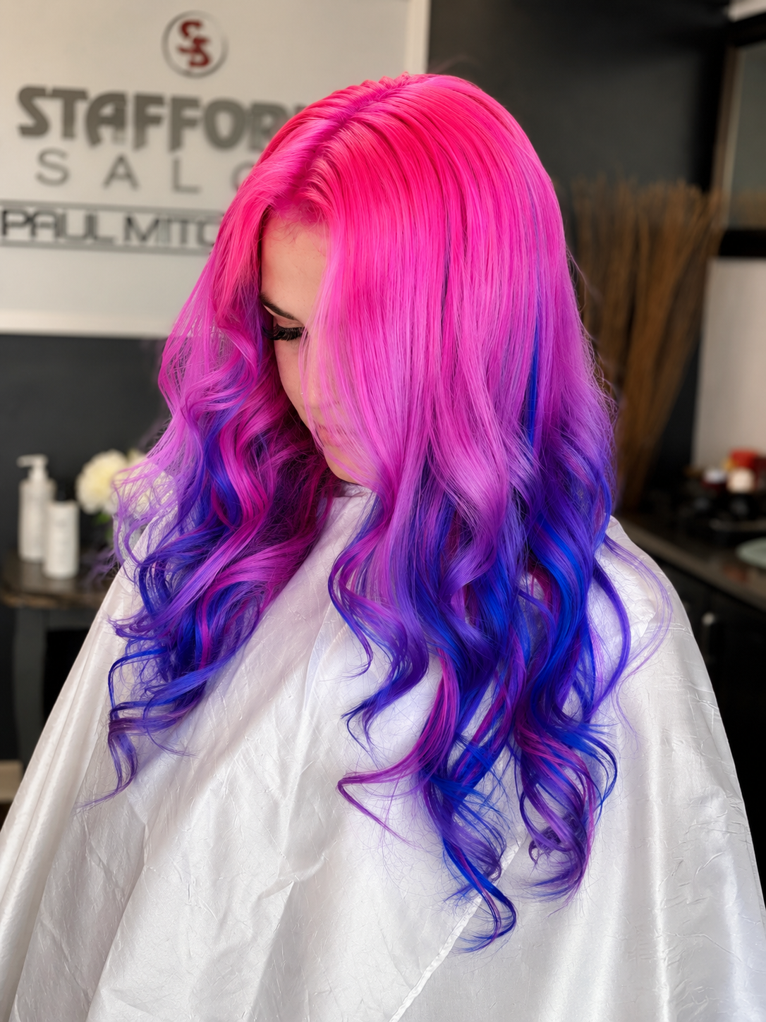 A woman with long, wavy hair in vibrant pink, purple, and blue colors at a hair salon.