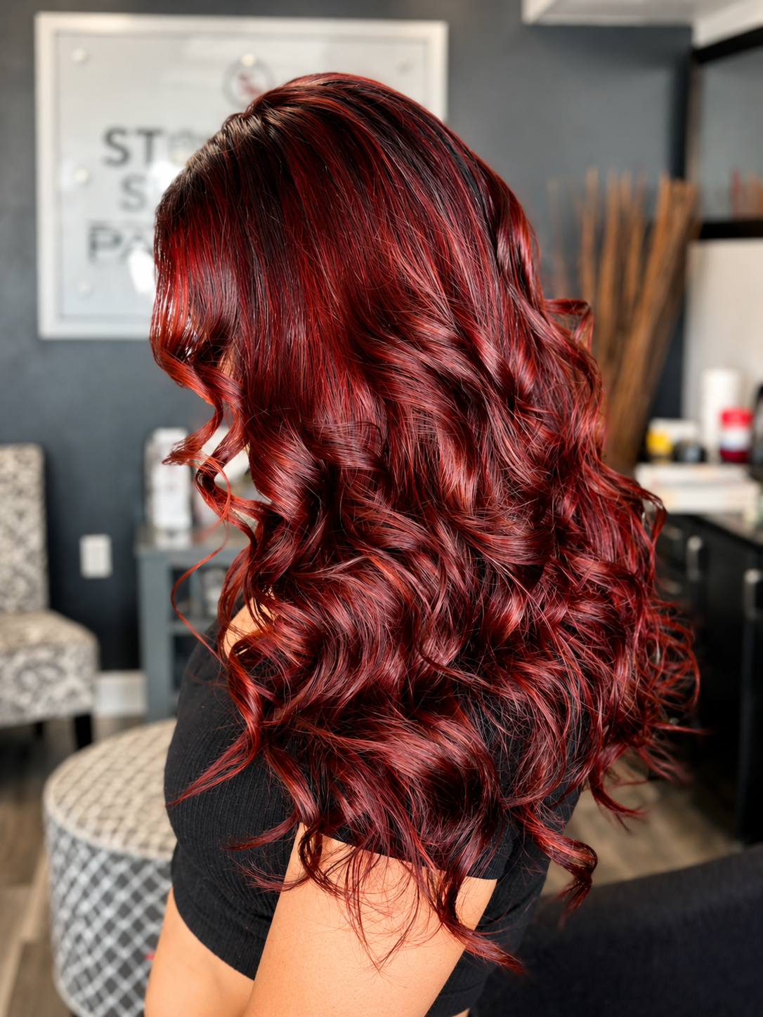 Side view of a woman with long, curly, vibrant red hair in a salon.