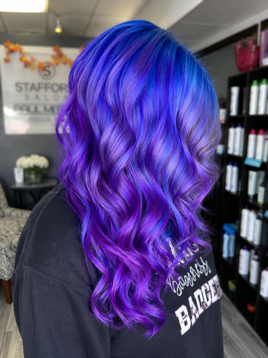 Woman with long, wavy hair dyed in shades of purple and blue, inside a salon.