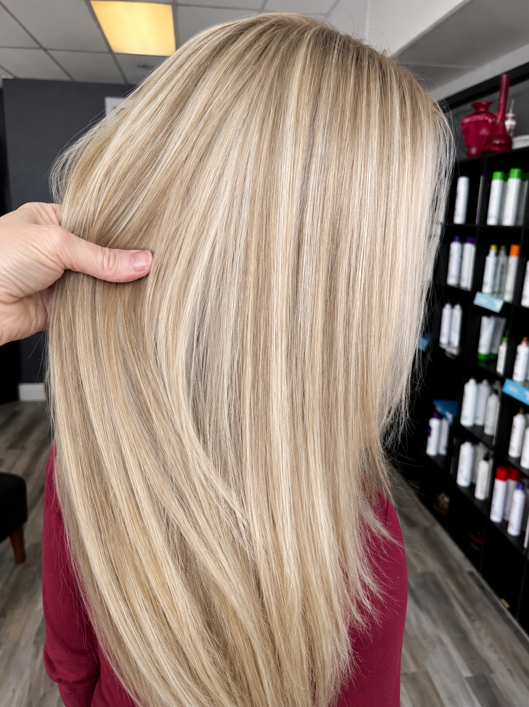 Close-up of a woman with long, straight blonde hair being styled or examined at a hair salon.