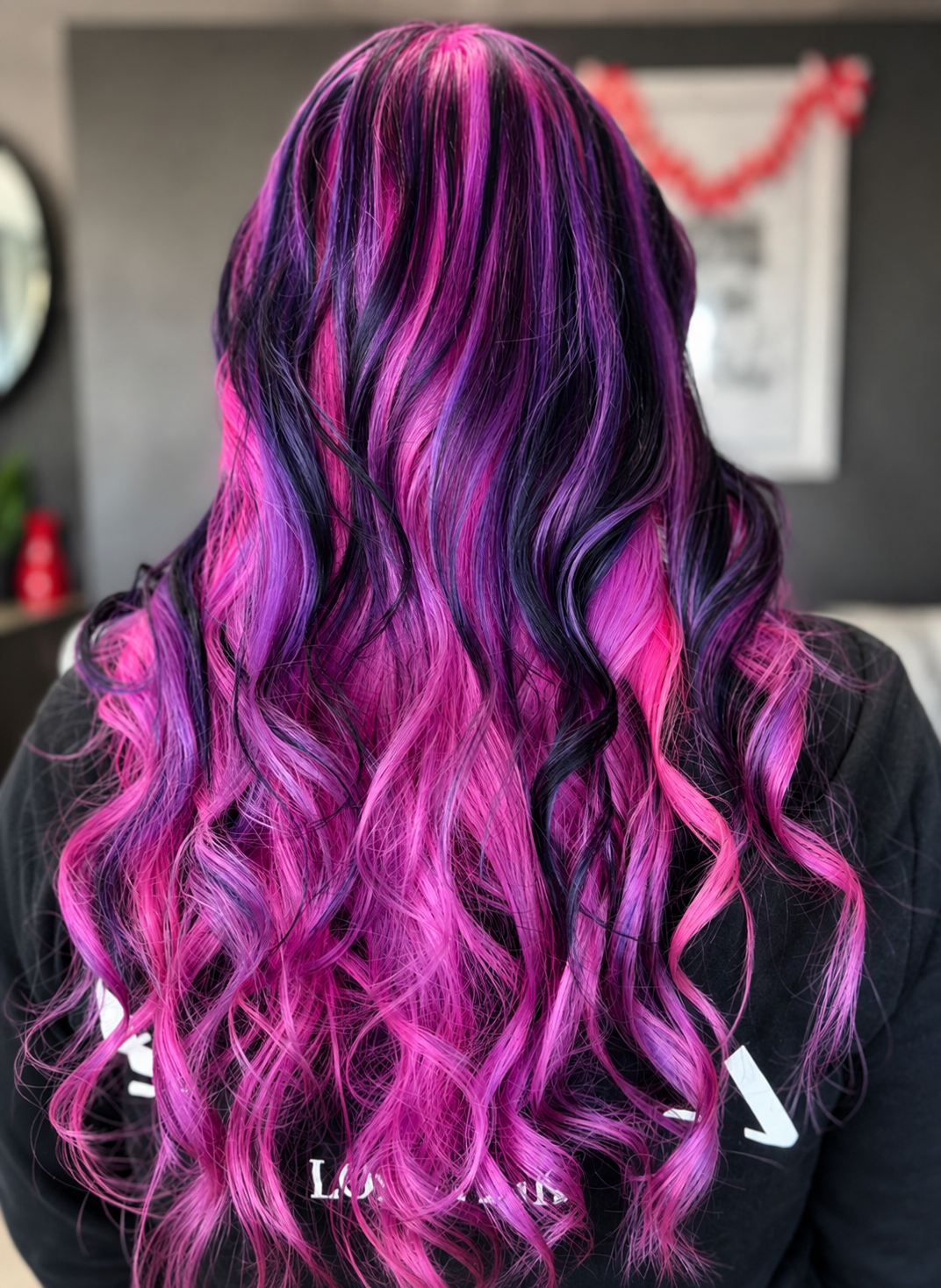 Back view of a person with long, wavy hair dyed in shades of pink, purple, and black.