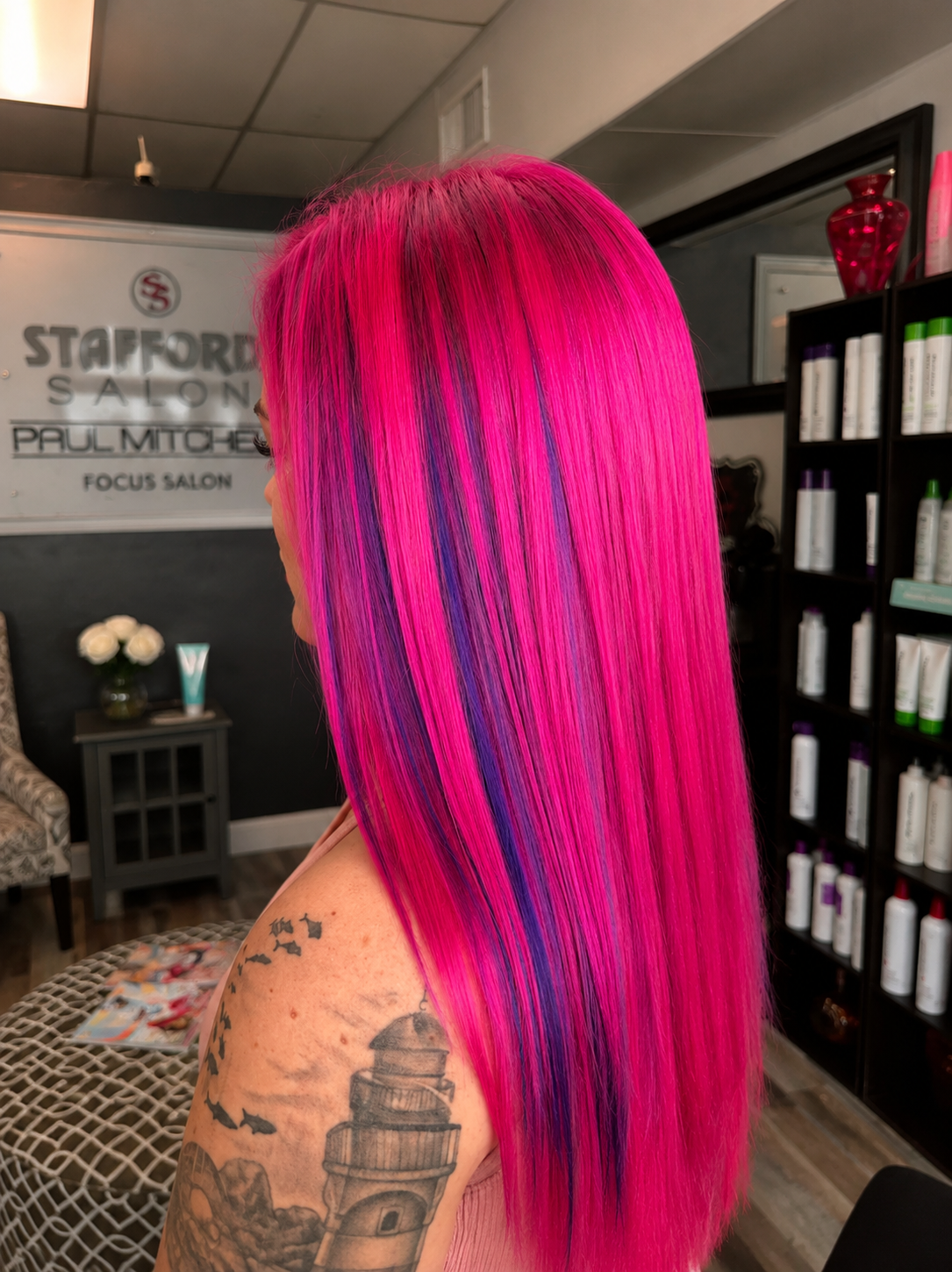 Side view of a woman with long, straight, bright pink hair with purple streaks, inside a salon.