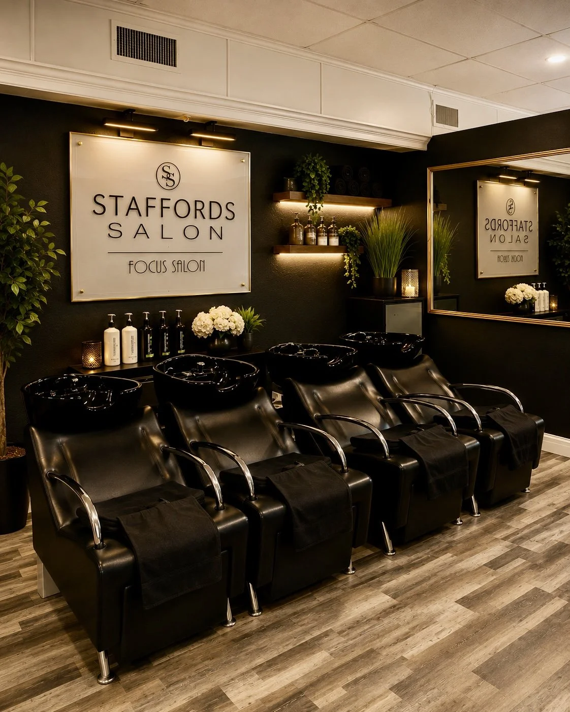 Hair washing stations with black sinks, black chairs, mirror, and decorative plants at Staffords Salon.