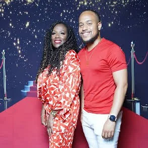 Kim and Ja'Von man and woman posing together on a red carpet with starry background and velvet ropes.