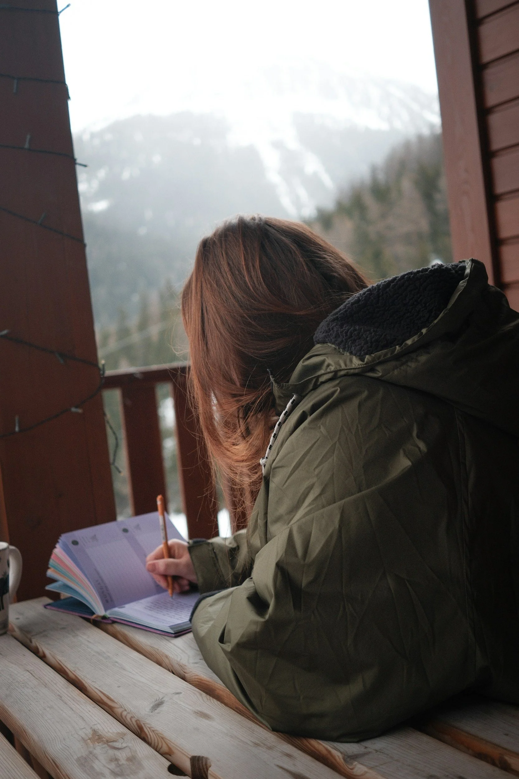 Person writing in a journal while seated on patio.
