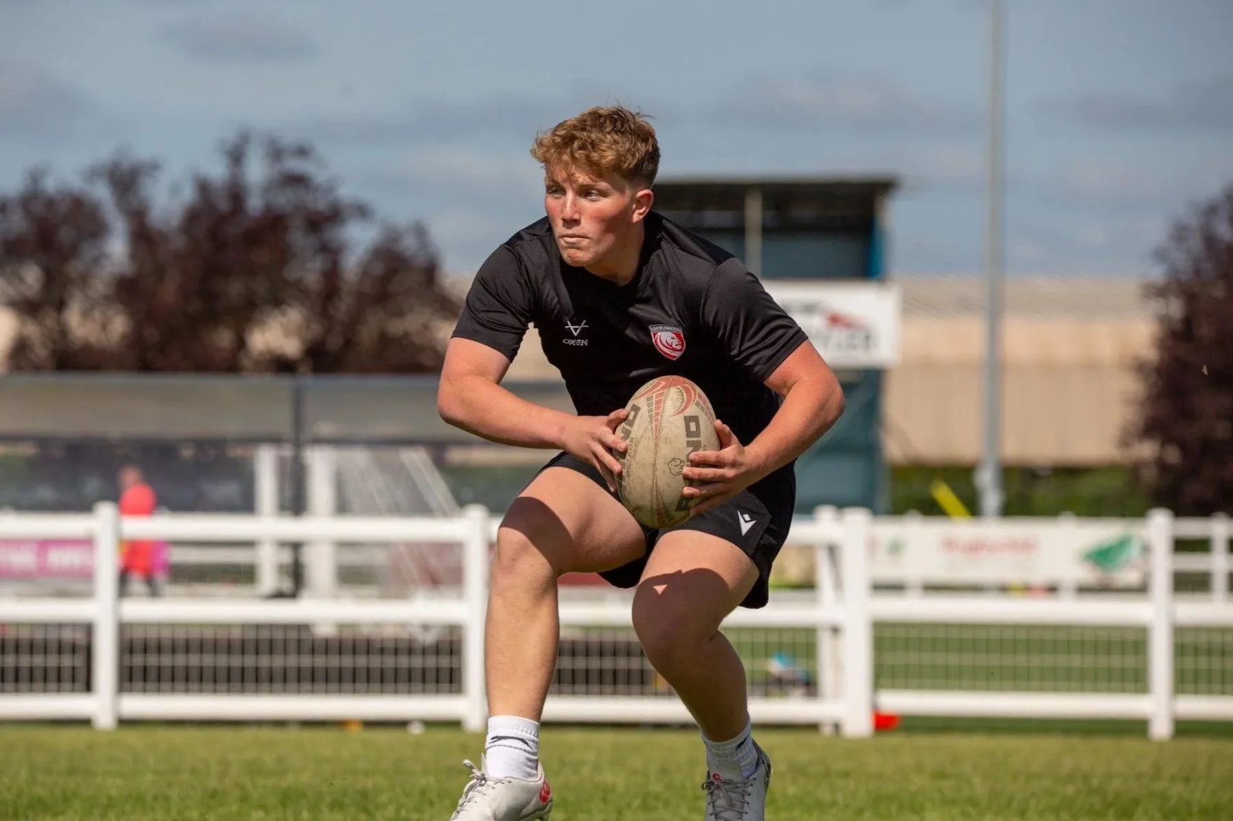 A young rugby player in a black uniform holding a rugby ball on a field during a game.