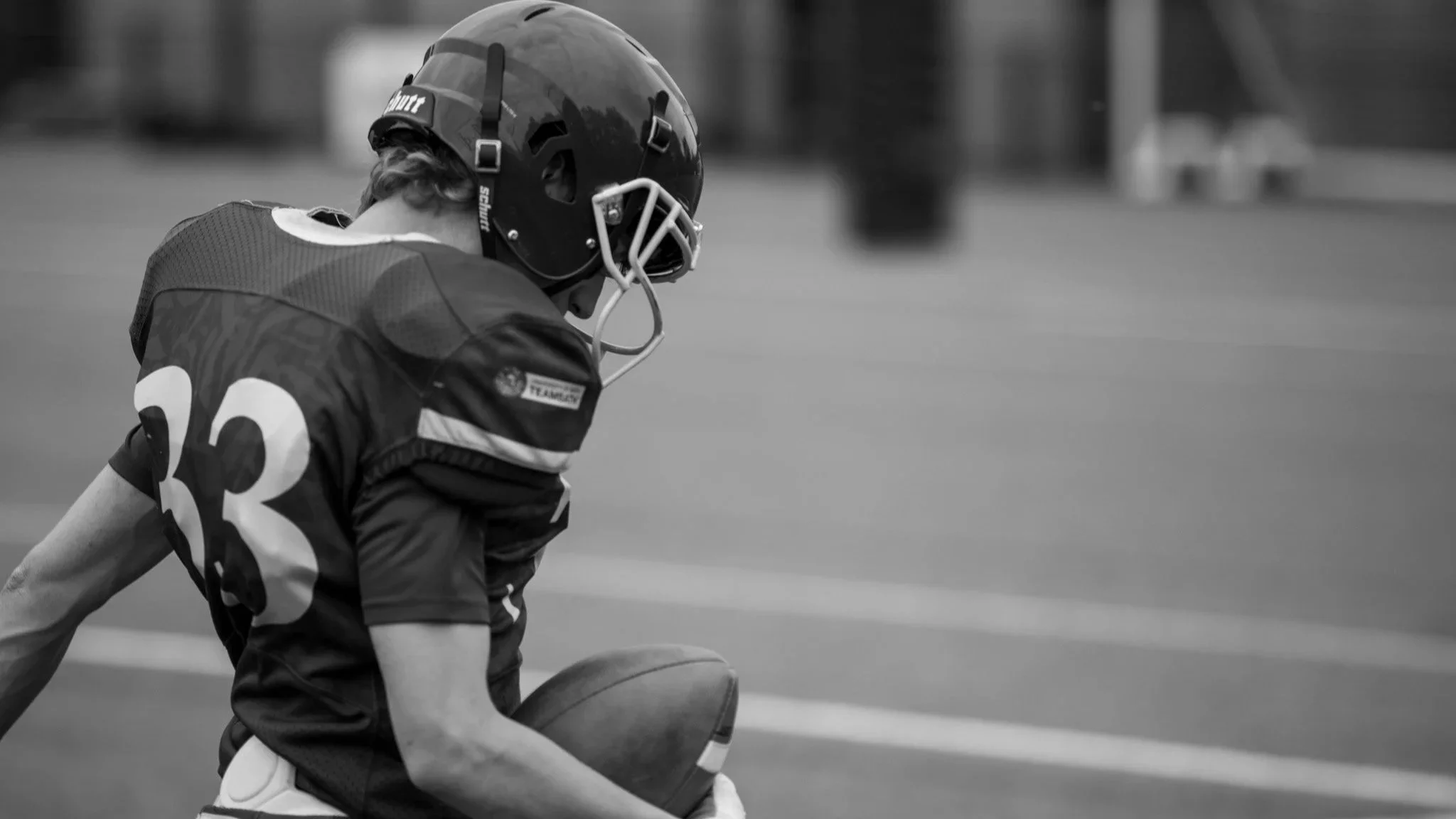 A young football player in uniform crouching on the field with a football, wearing a helmet and number 22 jersey, during a game or practice.