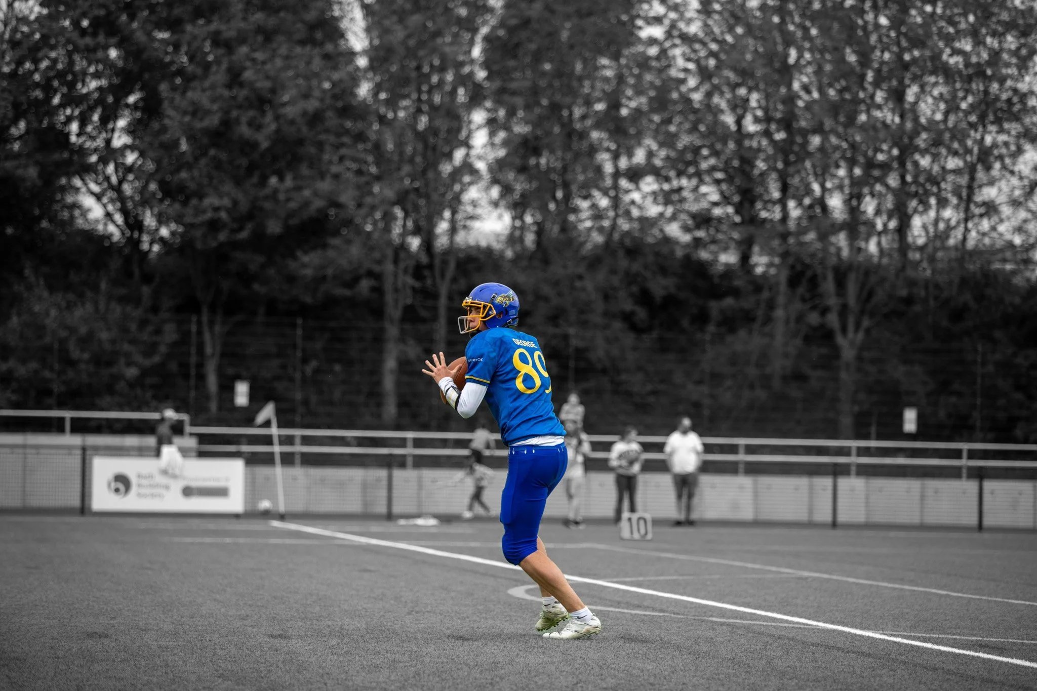 A football player in a blue uniform with the number 80 is preparing to throw a pass on the field, with other players and officials in the background at a stadium.