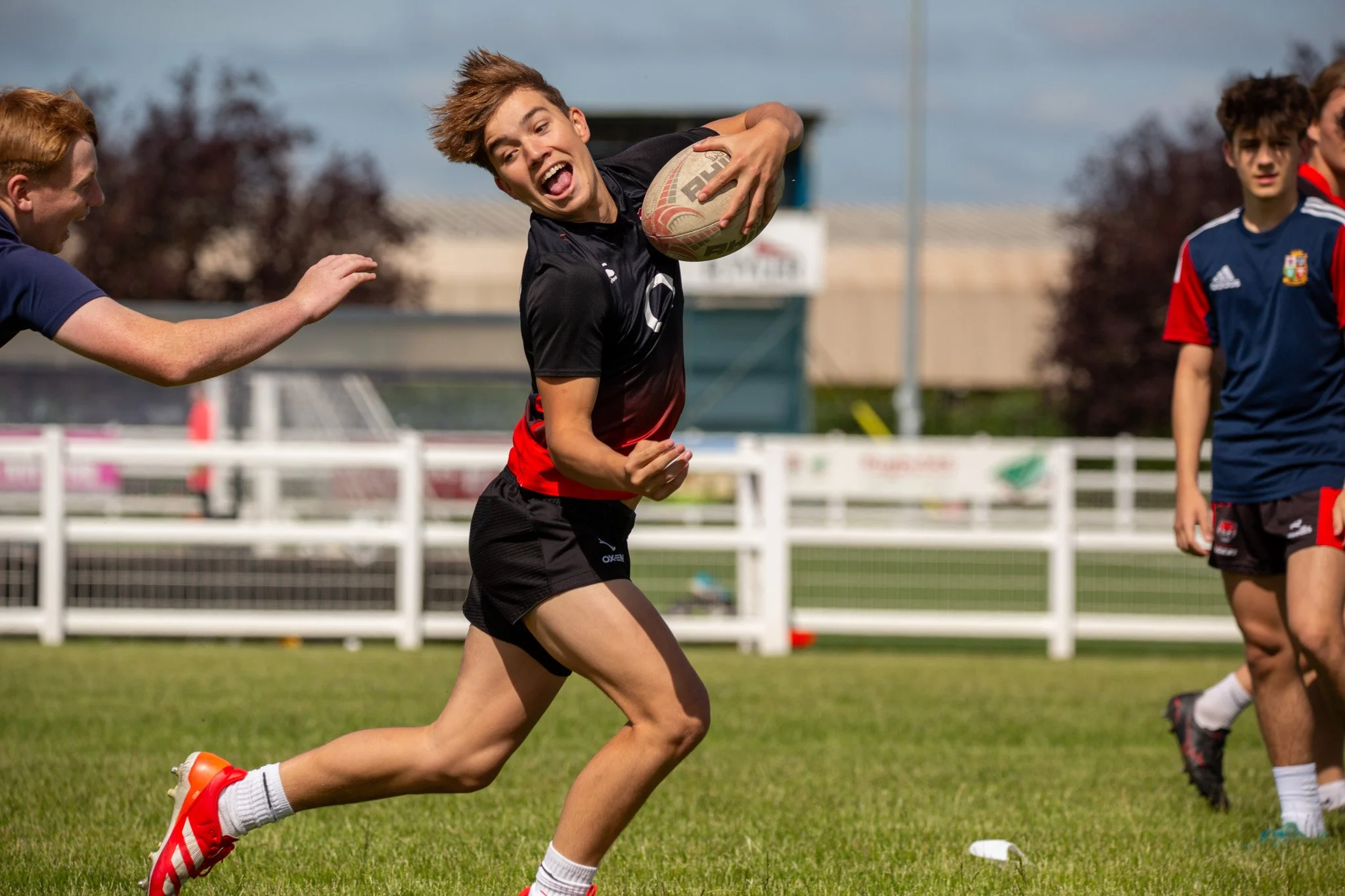 Young person running with rugby ball during practice on field, accompanied by other players.
