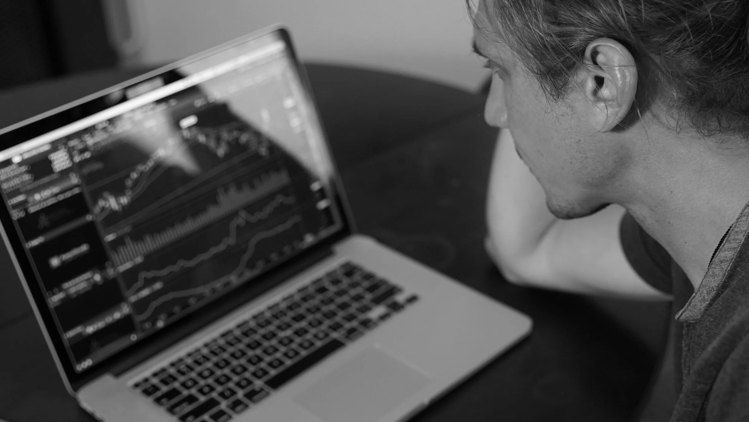 A person with short hair is working on a laptop displaying financial graphs and charts.