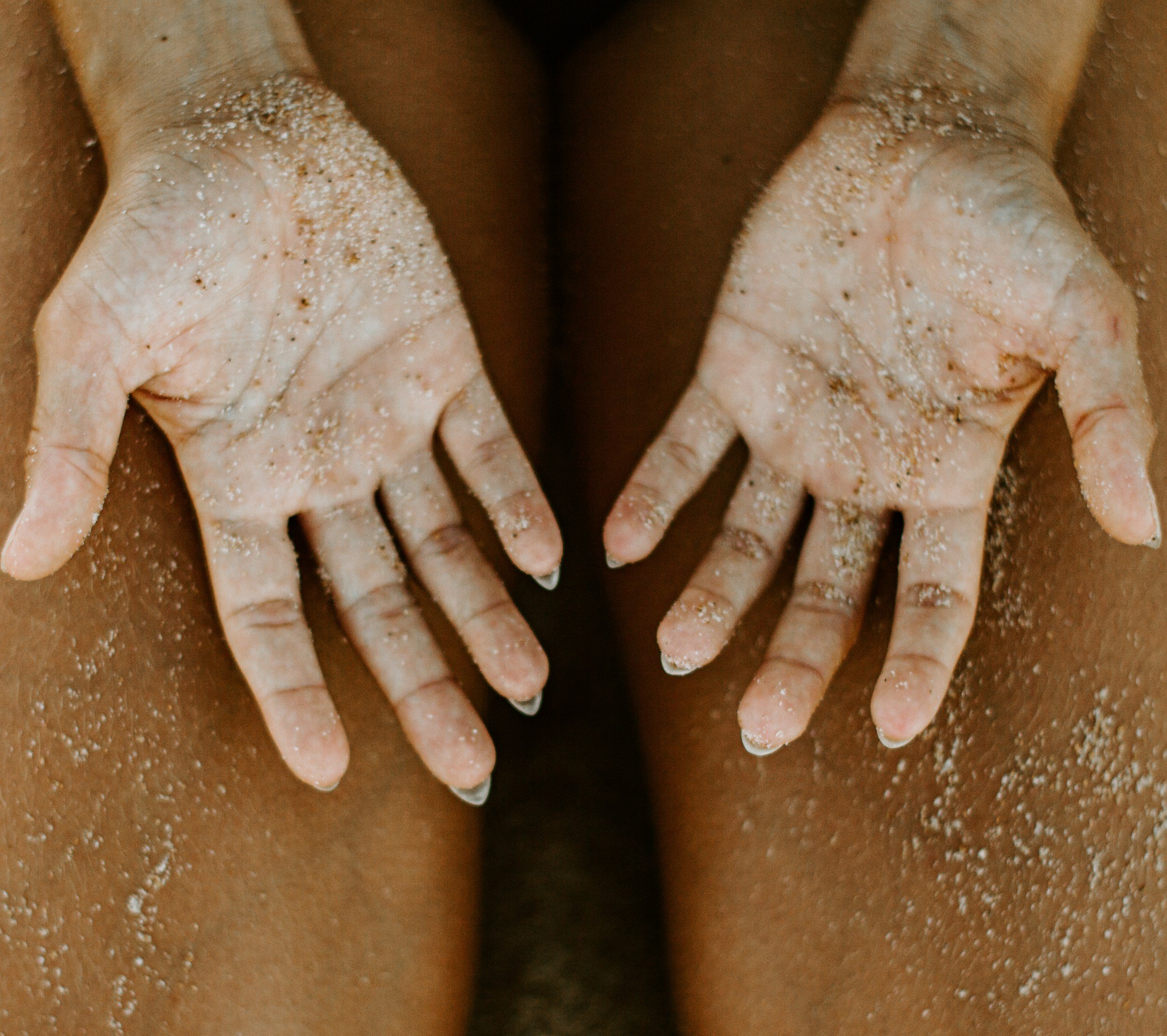 Close-up of two fingers pressed against a person's skin, with white powder sprinkled on the fingers and skin.