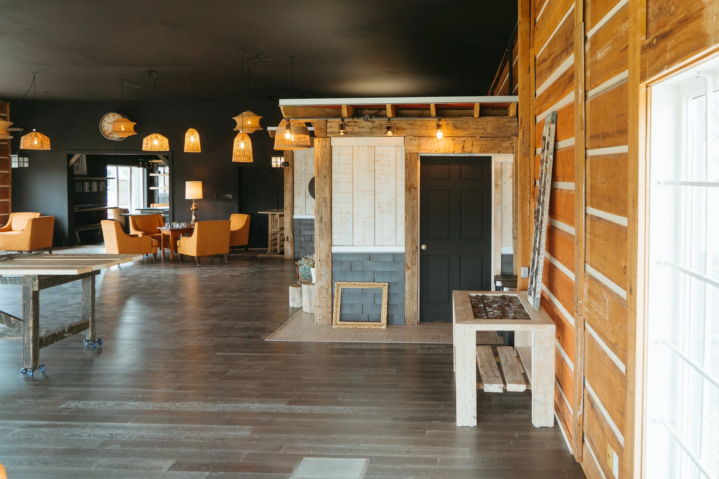 The interior of a rustic-style building featuring warm lighting, wooden walls, and modern furniture including chairs and tables, with a dark ceiling.